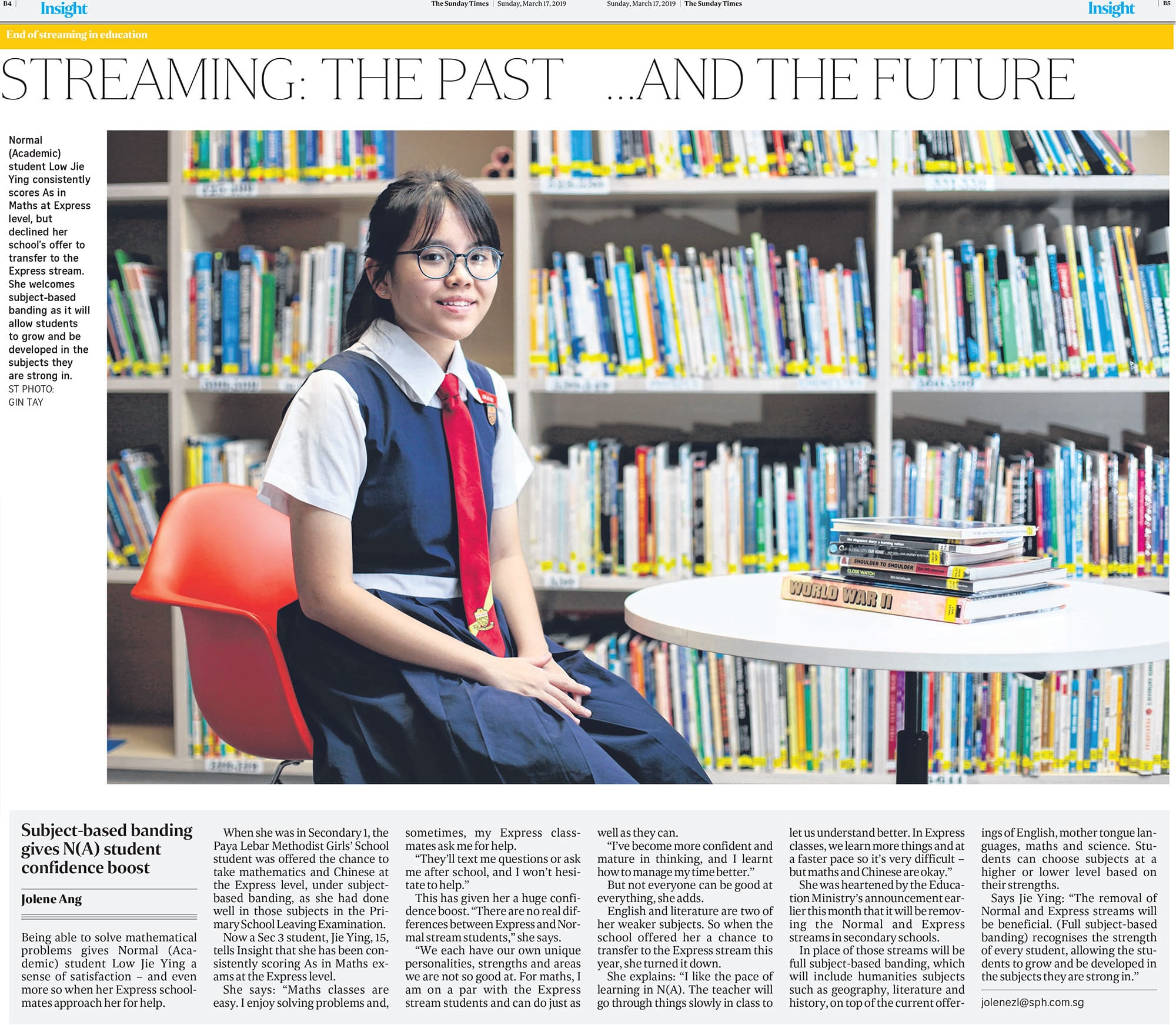 A young girl in school uniform sits smiling in a library, surrounded by bookshelves, in a Sunday Times article.