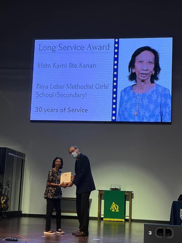 Two people on stage exchange a certificate below a screen displaying a Long Service Award for 30 years of service.