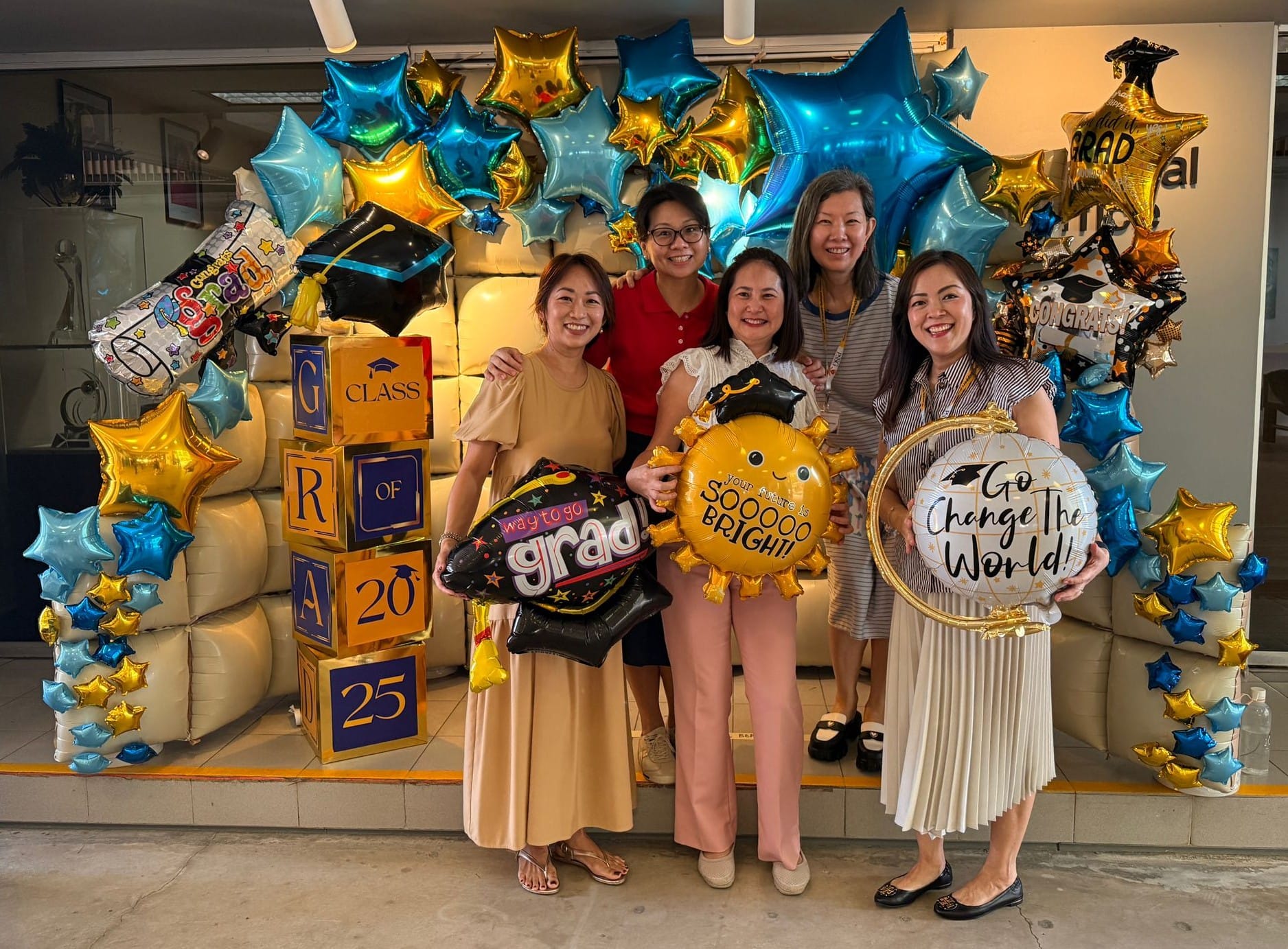 Five smiling women pose with graduation balloons and Class of 2025 decorated boxes at a graduation celebration.