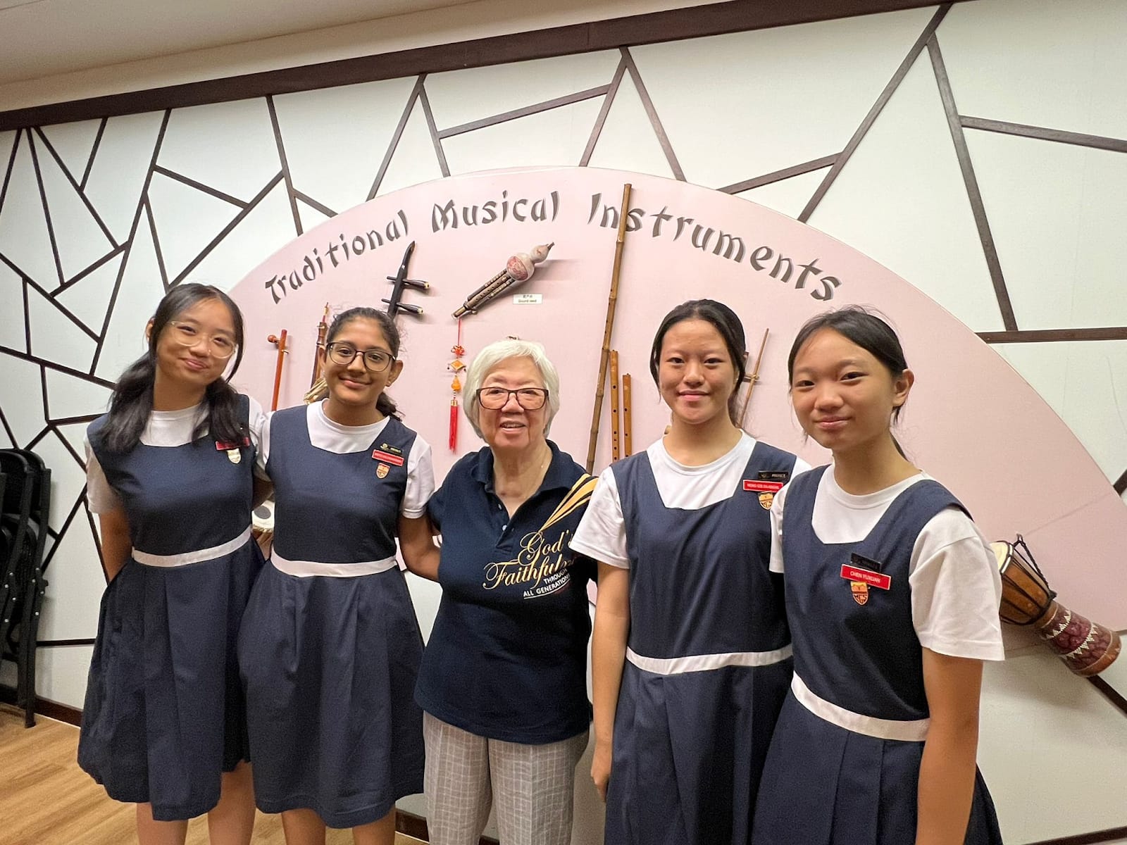 Five people pose in front of a Traditional Musical Instruments display with various instruments mounted on the wall.