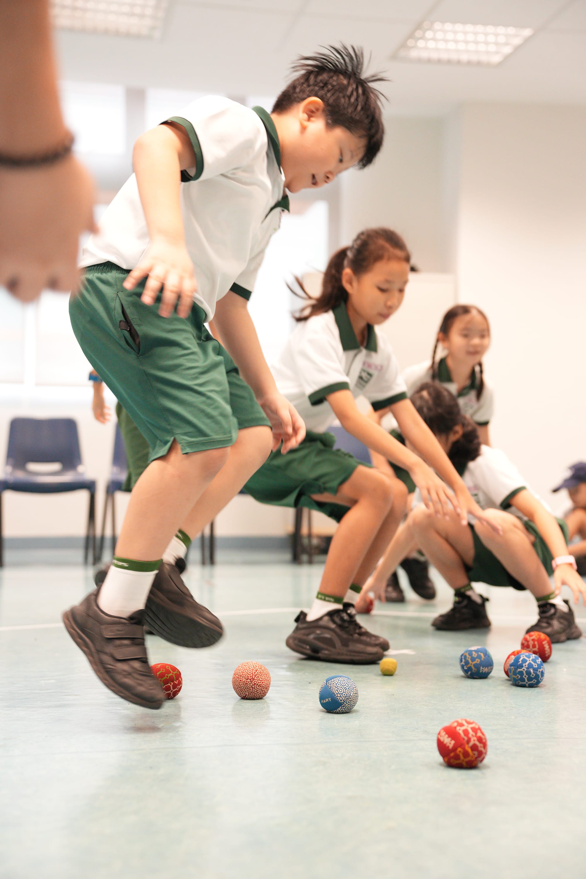 Students take part in a modified sports station, carefully collecting and moving coloured balls while developing balance, coordination, and teamwork.