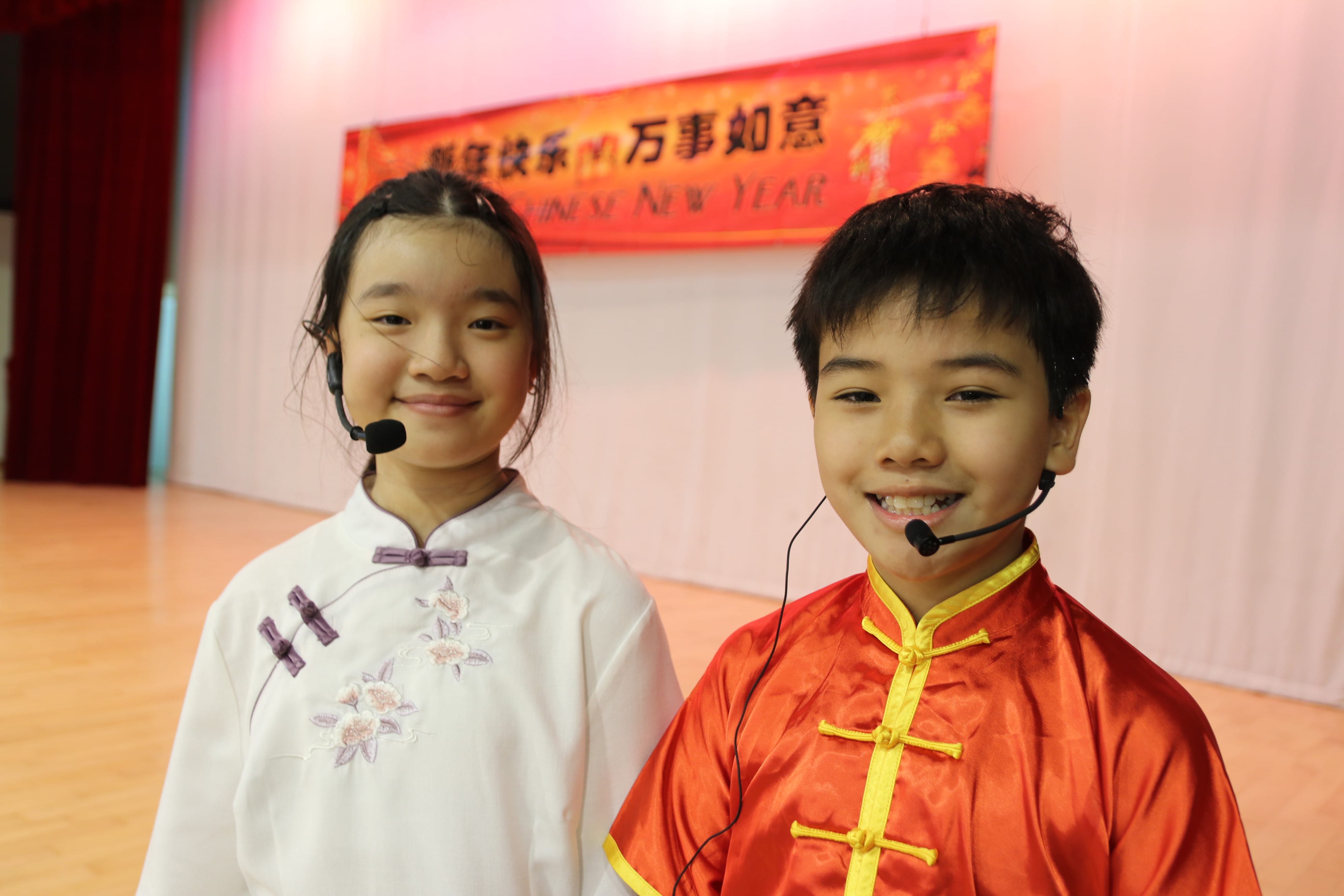 Two student emcees dressed in traditional Chinese costumes host the school's Chinese New Year celebration on stage.