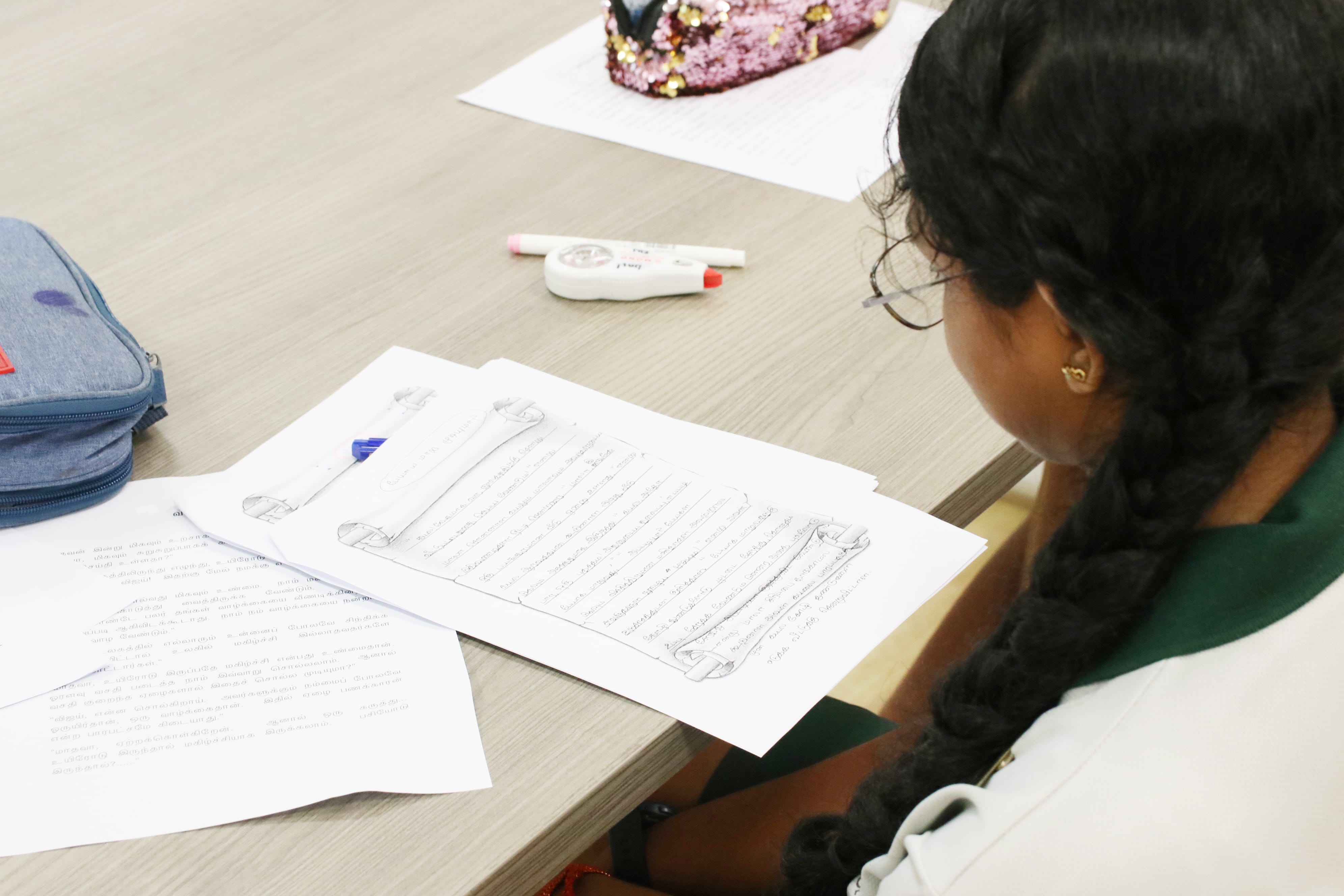 Student reading and reflecting on her creative writing piece during a workshop focused on developing expressive language and storytelling skills.