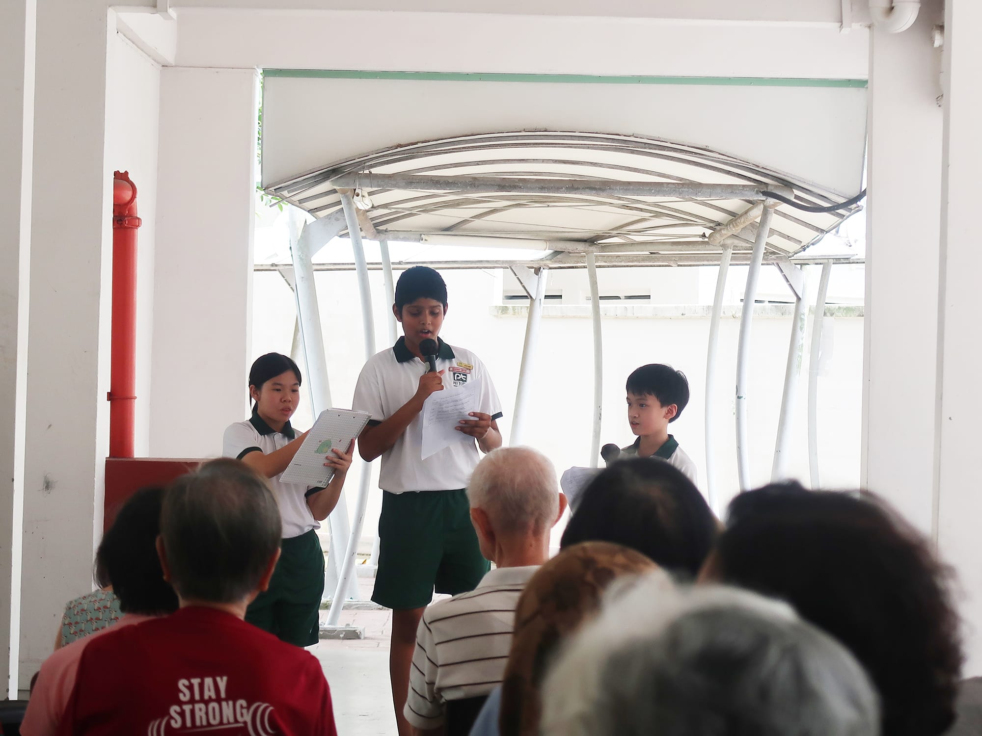 Students confidently present to a group of seniors, sharing messages and interacting with the audience during a visit to the activity centre.