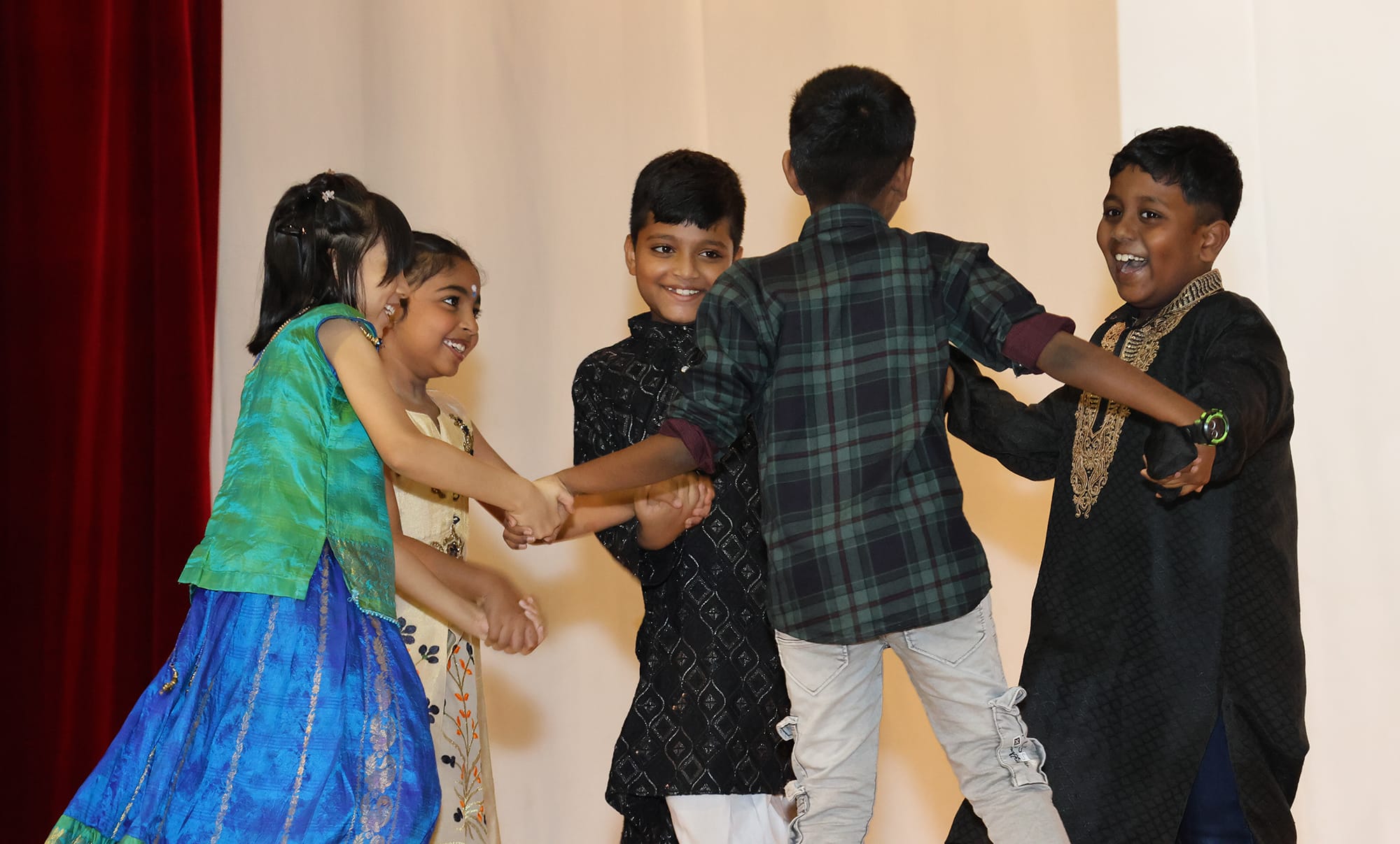 Students in traditional Indian attire perform together on stage, celebrating Deepavali through dance and teamwork.