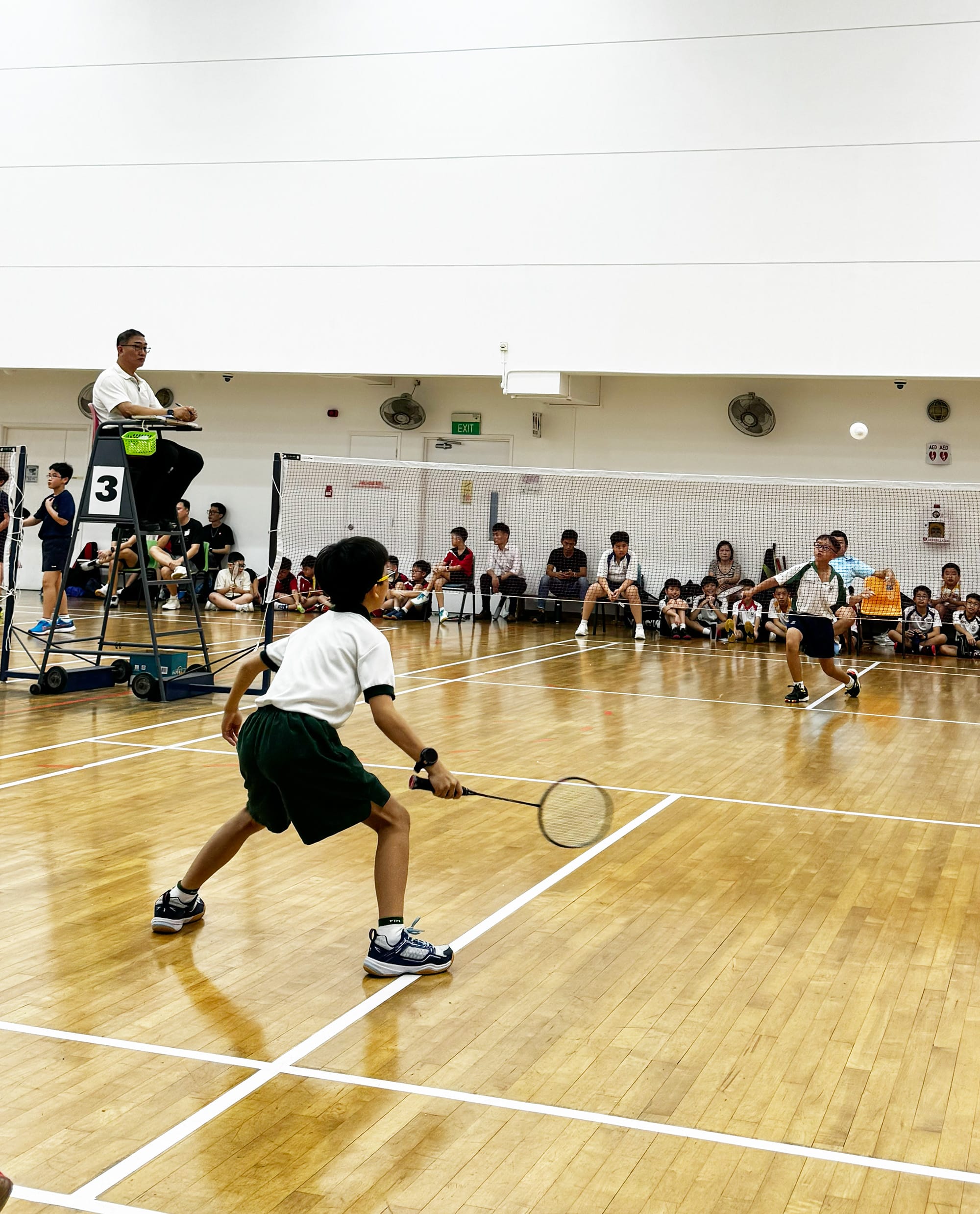 Students compete in a badminton match during a school competition, demonstrating agility, focus and sportsmanship.