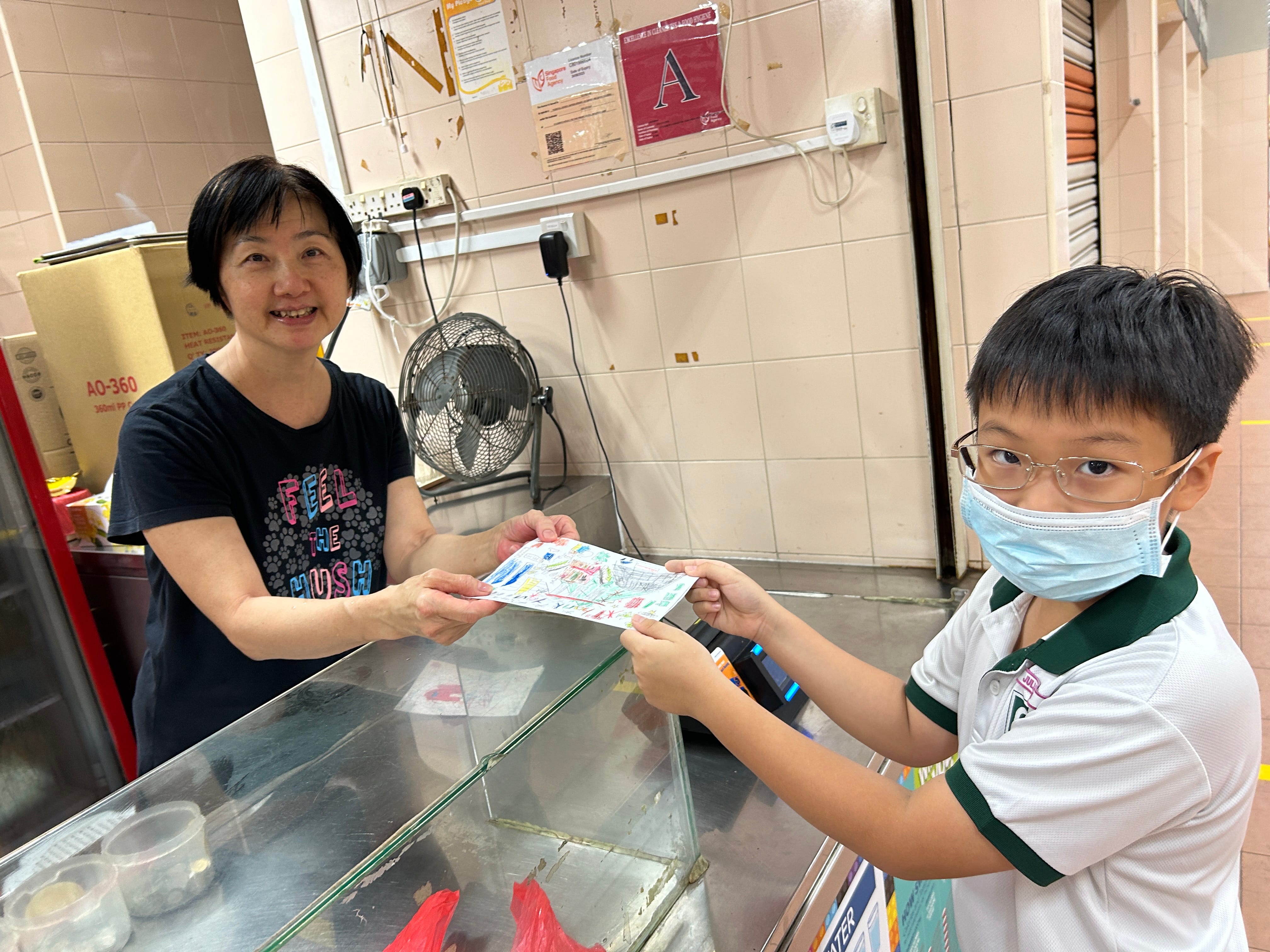 A student presents a handmade appreciation card to a canteen vendor, expressing gratitude for her care and service to the school community.
