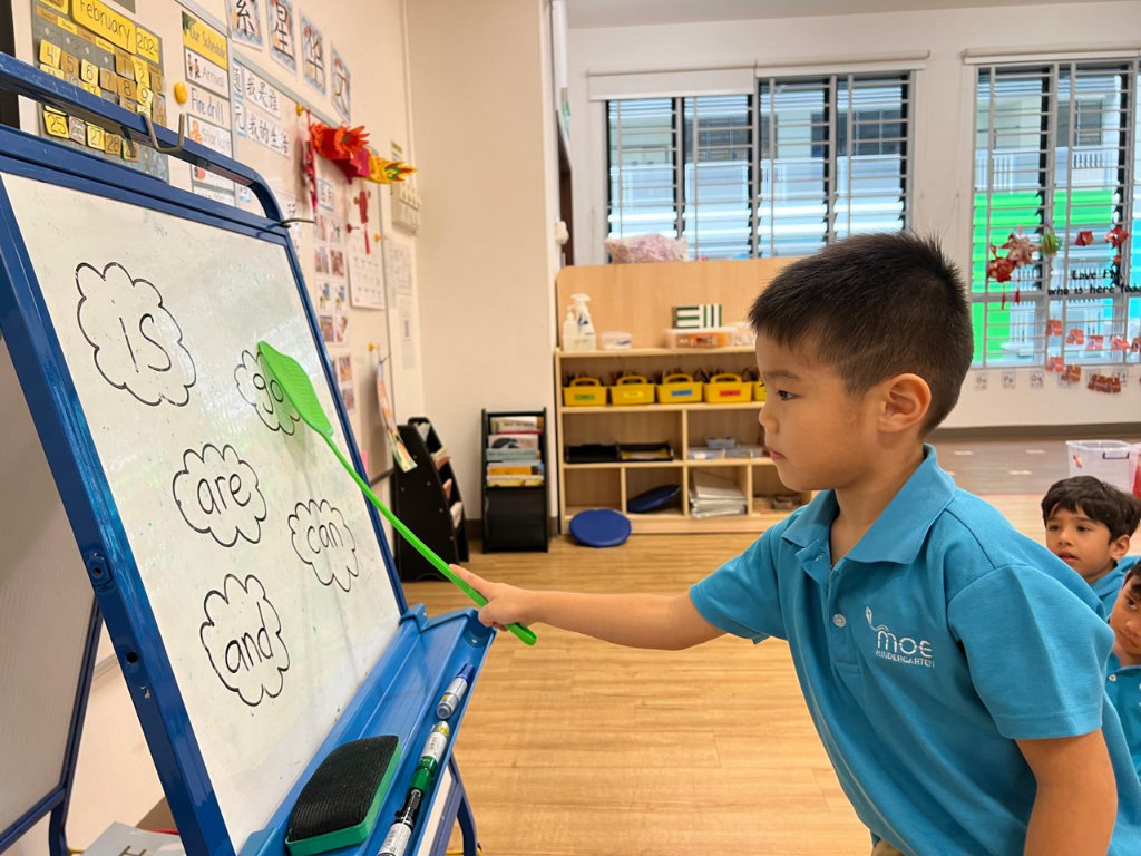 A kindergarten child points to sight words on a classroom whiteboard, building early reading skills through interactive word recognition.