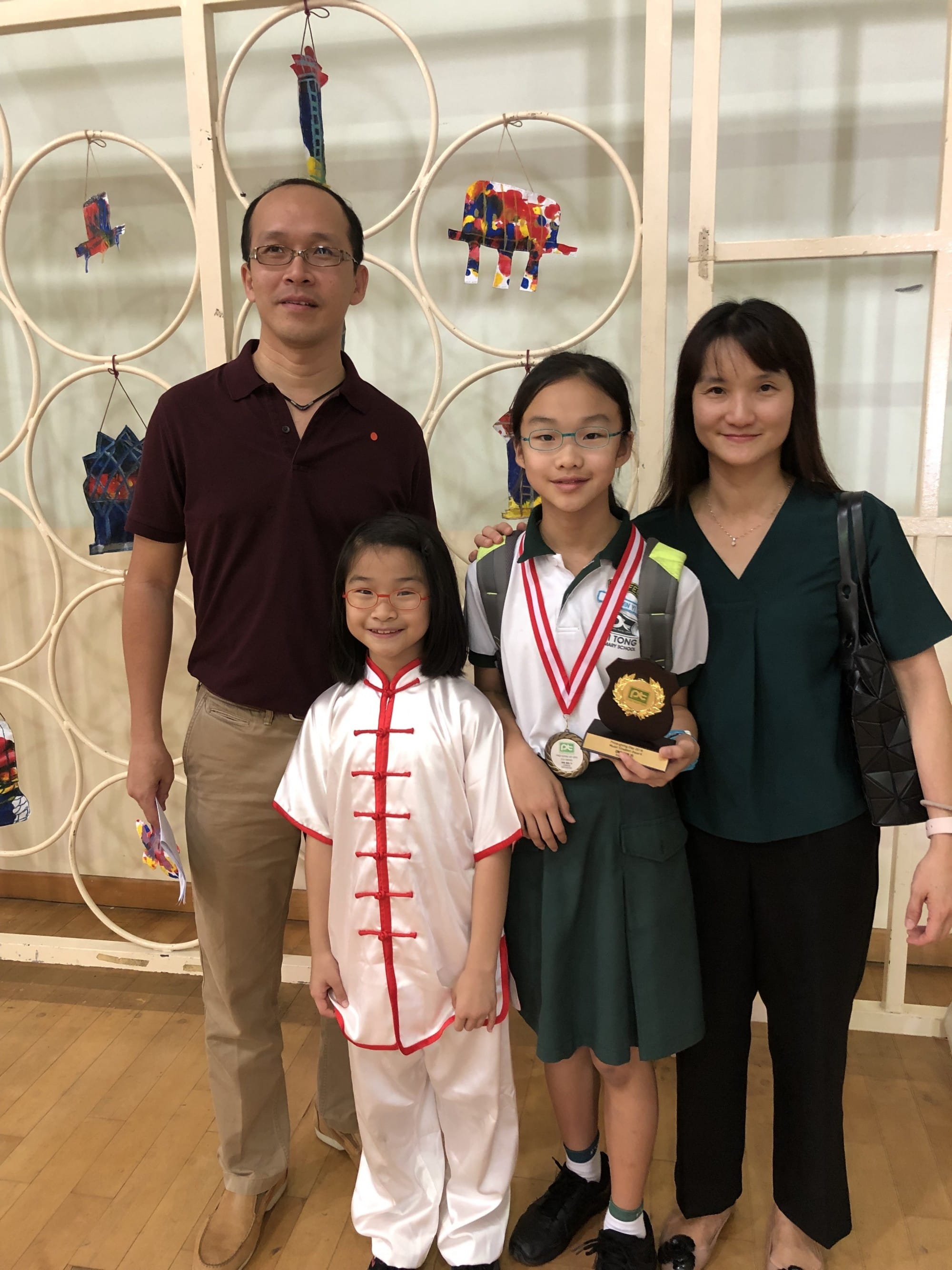 Two adults and two children pose indoors; one child in uniform holds a medal and a trophy.