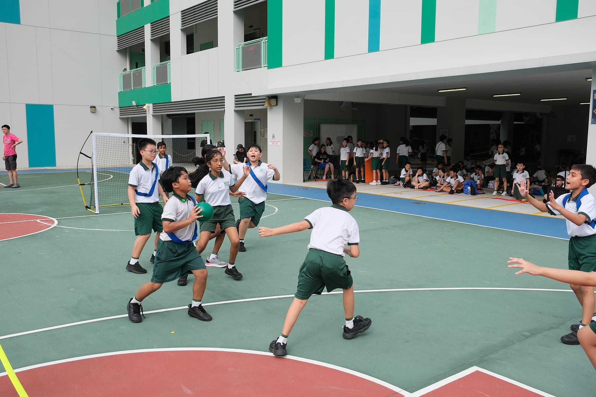 Students compete in a fast-paced captain's ball match, passing, defending, and working together as classmates watch from the sidelines.