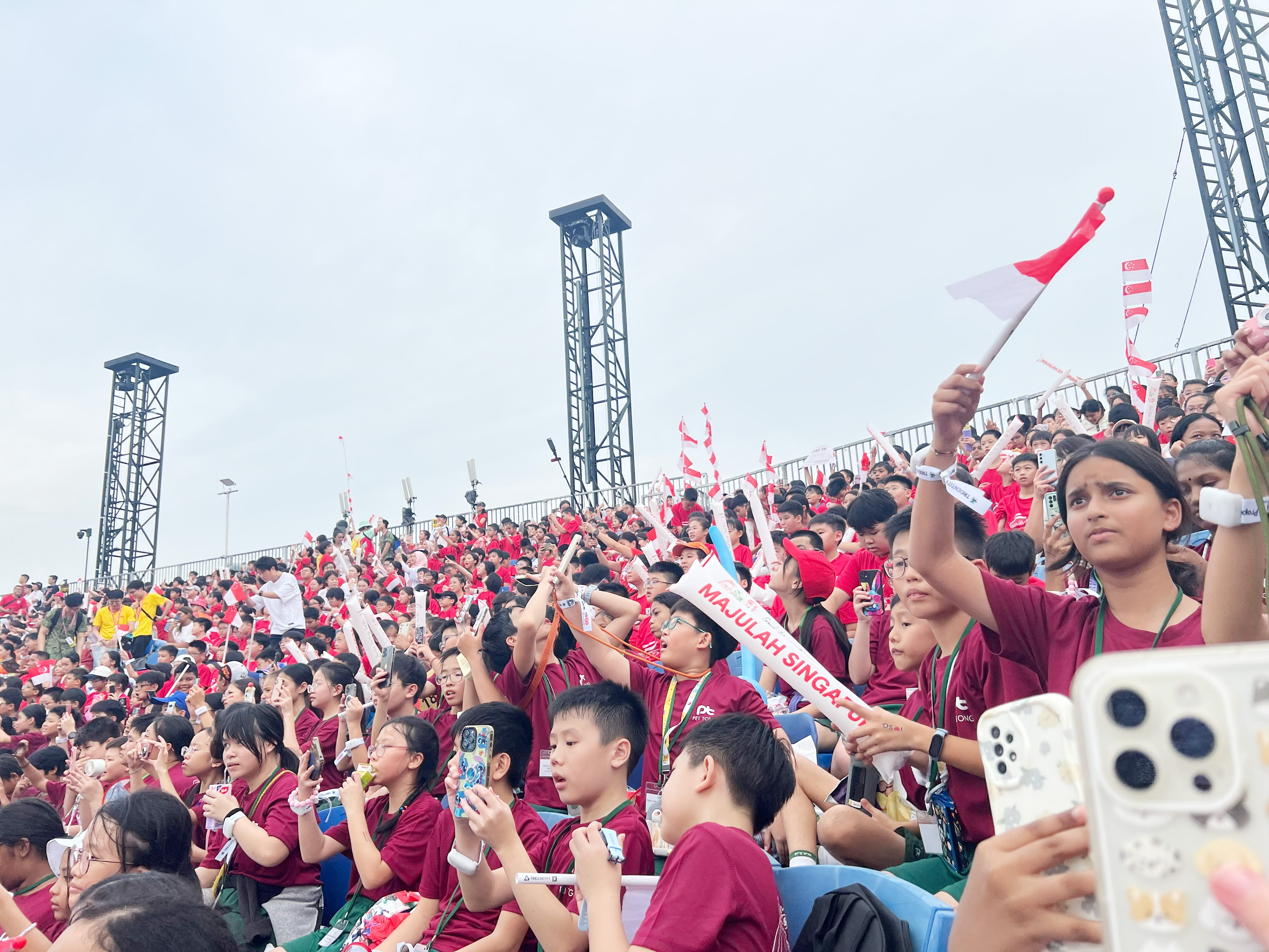 Primary 5 students wave Singapore flags and cheer enthusiastically during the National Education Show, expressing national pride and unity.