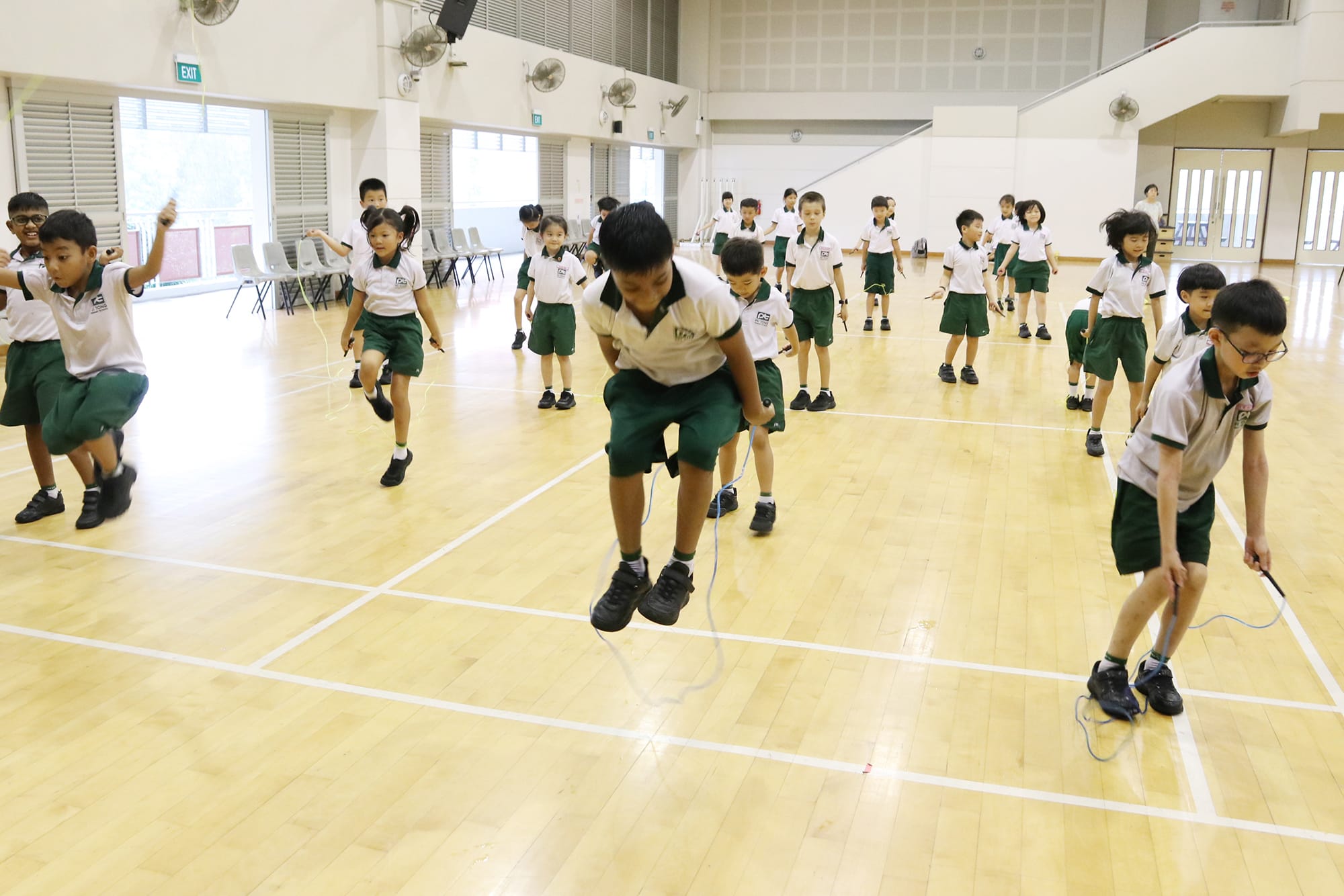 Primary 1 and Primary 2 students practise skipping in the school hall, developing coordination, rhythm, and cardiovascular fitness through fun physical activities.