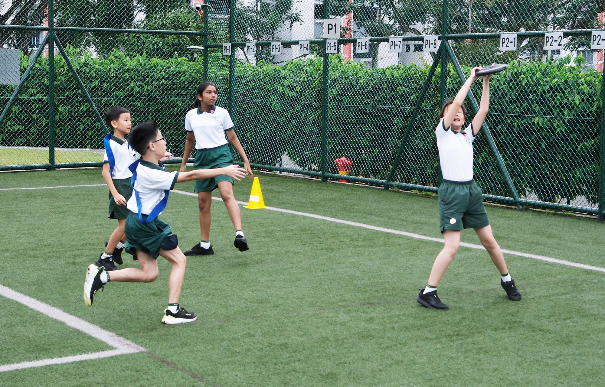 Students play an exciting game of Ultimate Frisbee on the field as one student jumps to catch the flying disc while teammates and opponents move into position to defend and support the play.