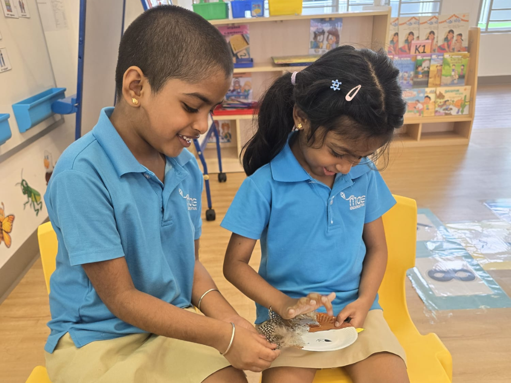 Two children investigate natural materials by observing and touching feathers and shells, encouraging curiosity and discussion during project work.