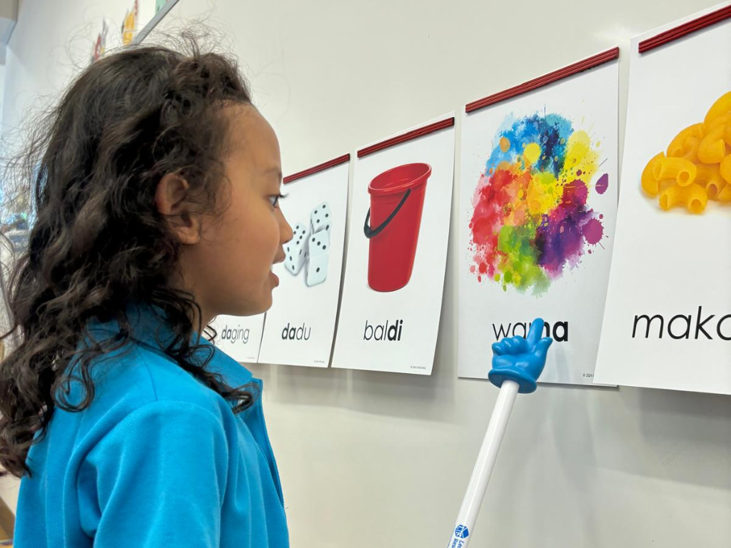 A child identifies and names everyday objects using picture cards, strengthening vocabulary and language skills in a meaningful local context.