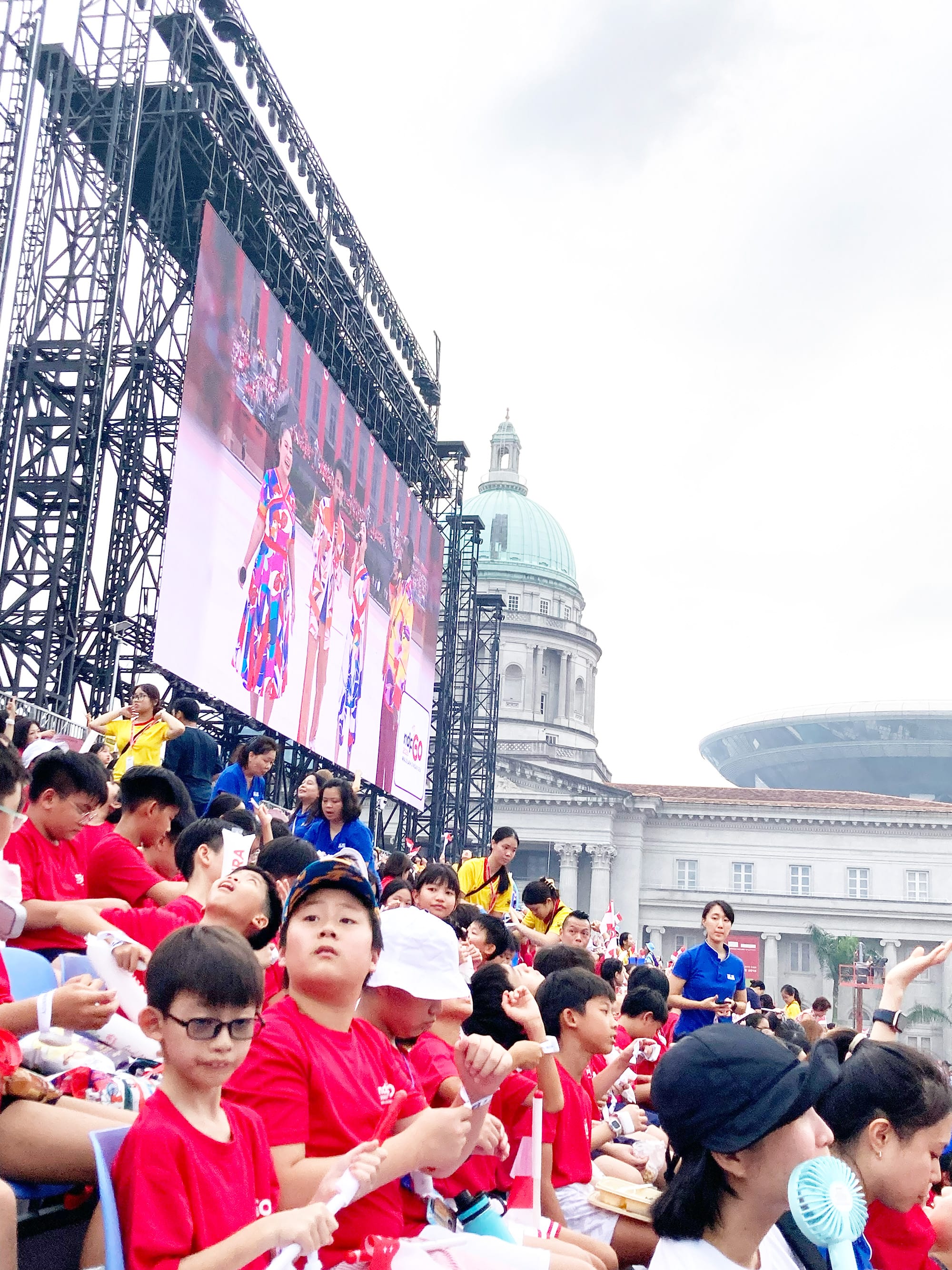 Primary 5 students in red school shirts gather at the National Education Show venue, eagerly waiting for the programme to begin.