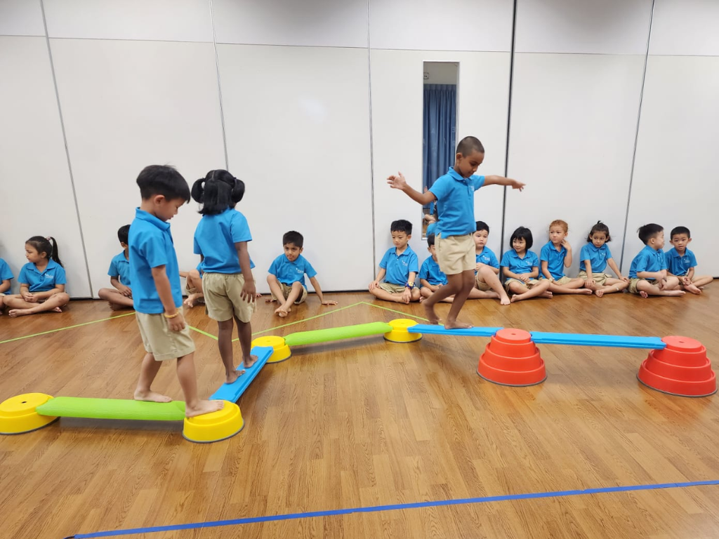 Children take turns balancing on an obstacle course, developing coordination, confidence and the ability to follow instructions through movement-based activities.