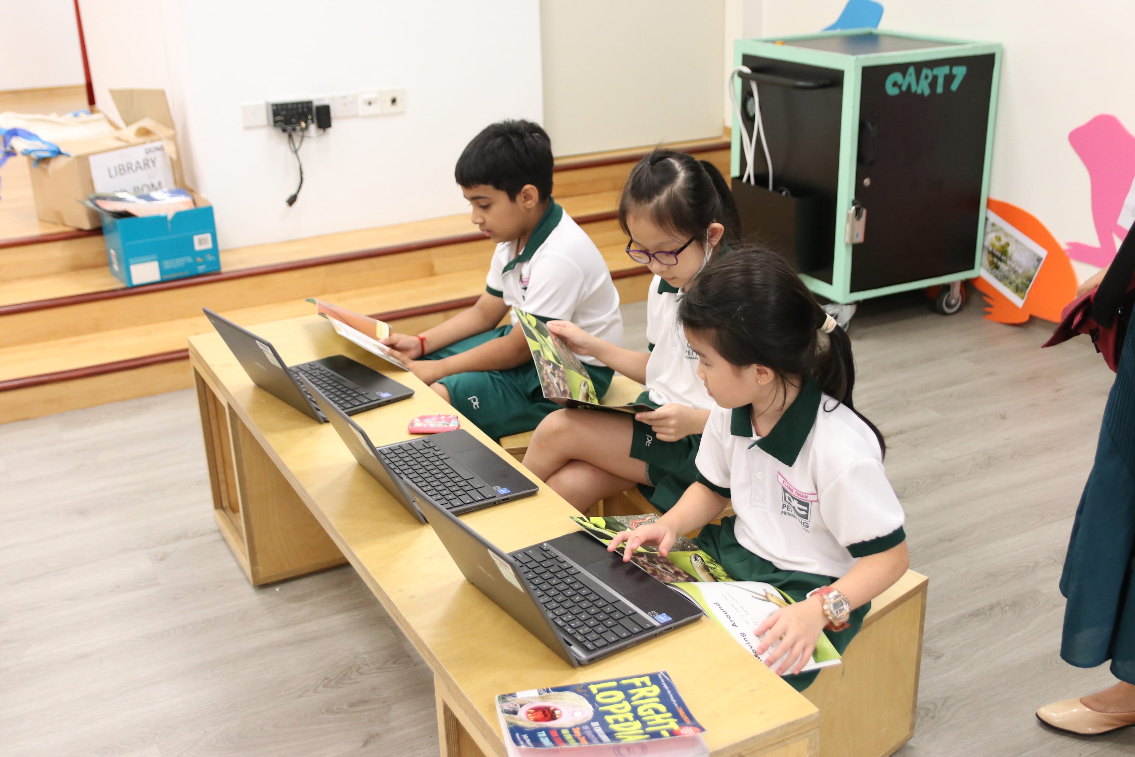 Three students using books and chromebooks during a storytelling activity, as they explore digital resources to support their learning and discussion.