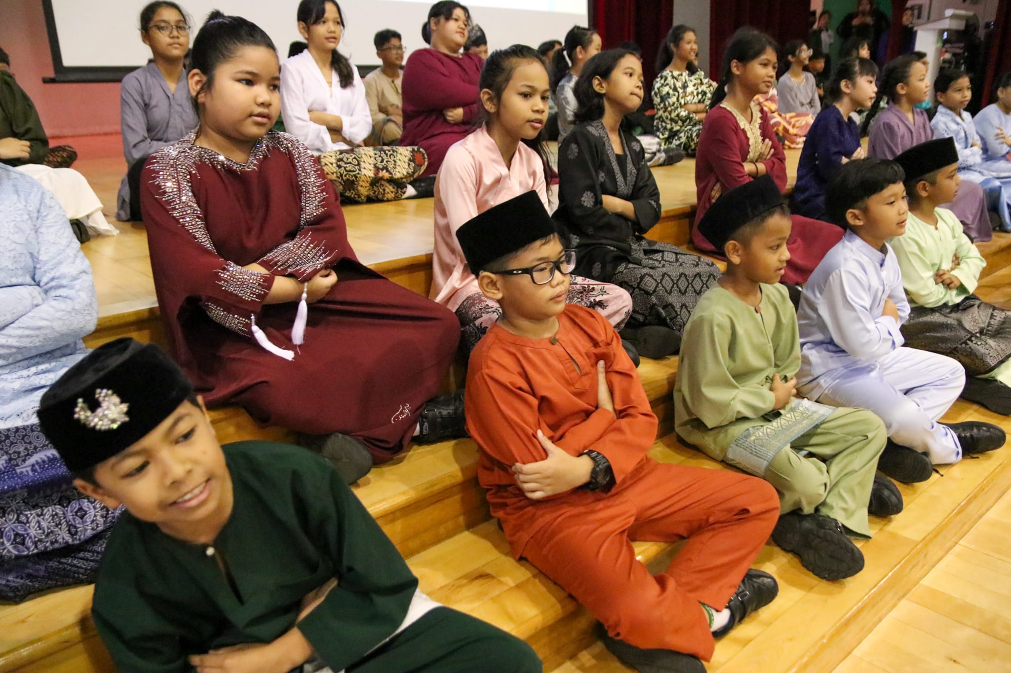 Students dressed in traditional Malay attire sit together during the school's Hari Raya celebration, learning about the festival and its cultural traditions.