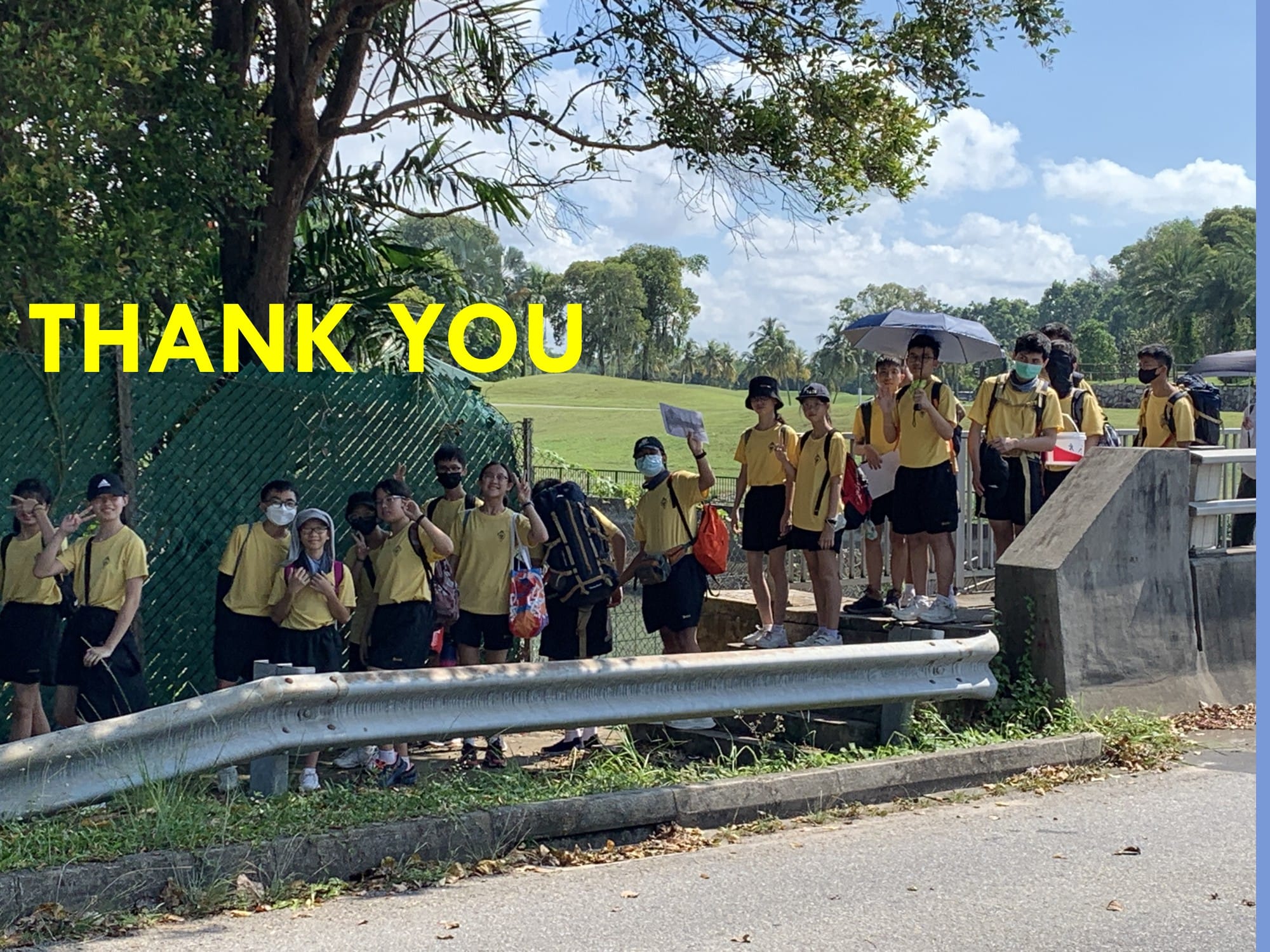 A group of students in yellow shirts and black shorts stand outdoors near a road with yellow text reading THANK YOU.