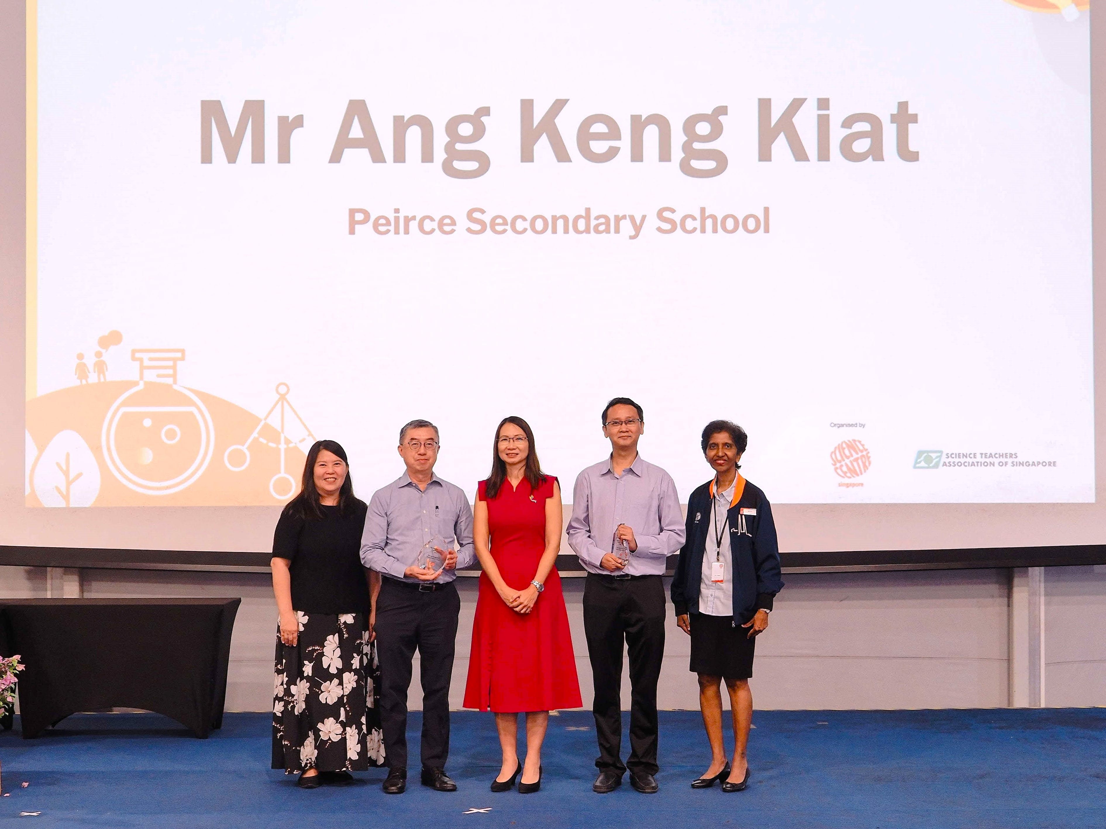 Five people stand on a stage in front of a screen displaying "Mr Ang Keng Kiat, Peirce Secondary School."