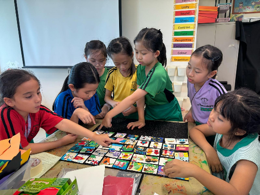 Six young children gather around a classroom table, sorting small colorful picture cards together.