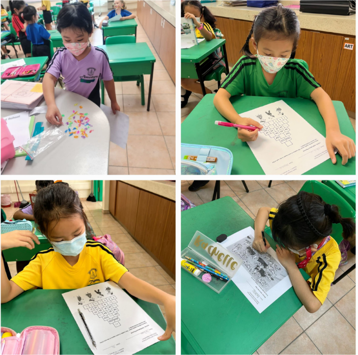 Four masked young students sit at green desks in a classroom, working on worksheets and craft activities.