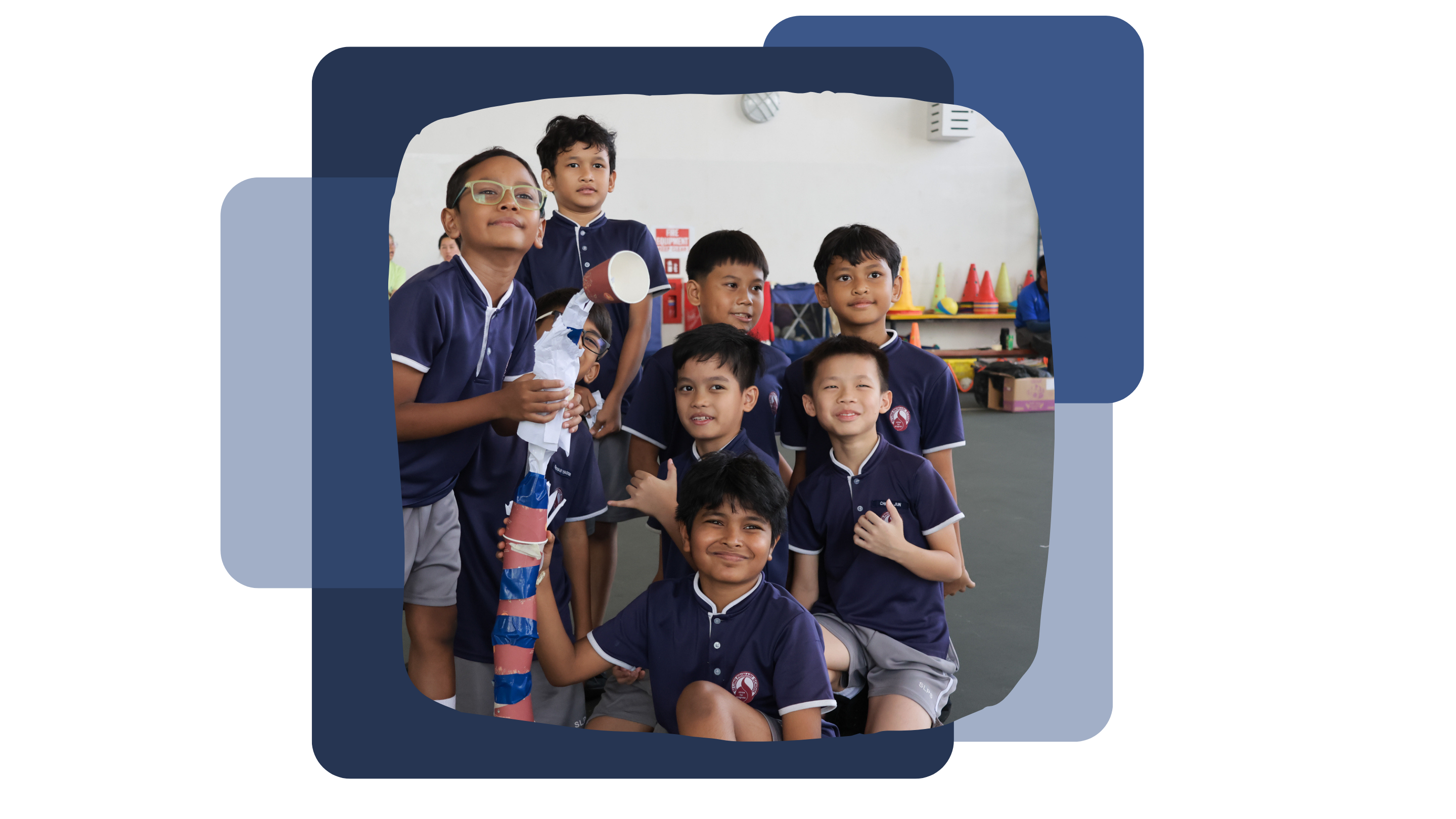 Seven young students in navy blue uniforms smile together indoors, with a colorful stacked cup tower beside them.