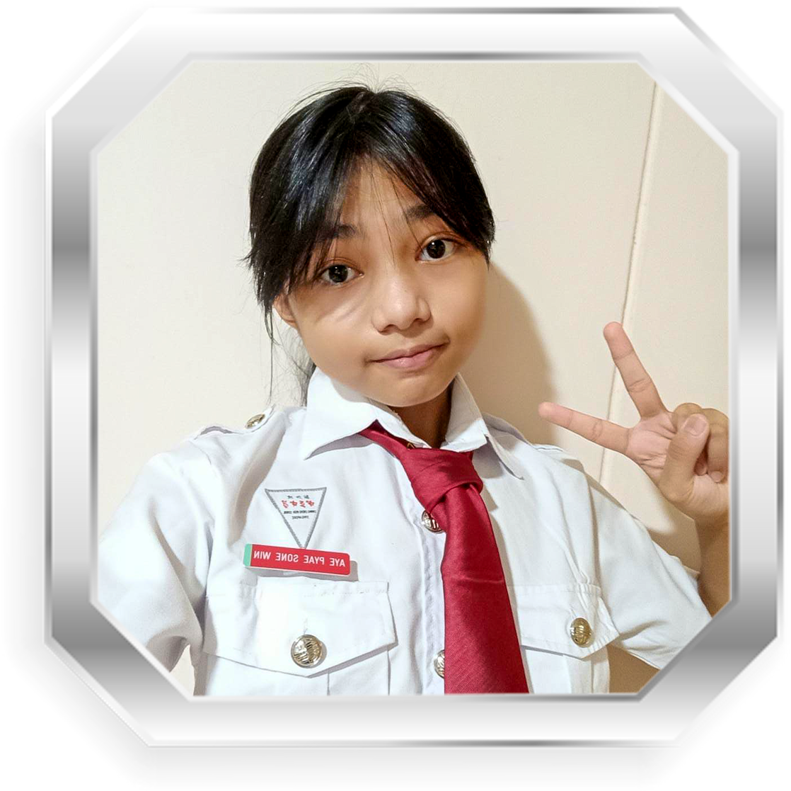 Young person in a white uniform with a red tie and name badge, making a peace sign gesture, framed in a silver octagon border.