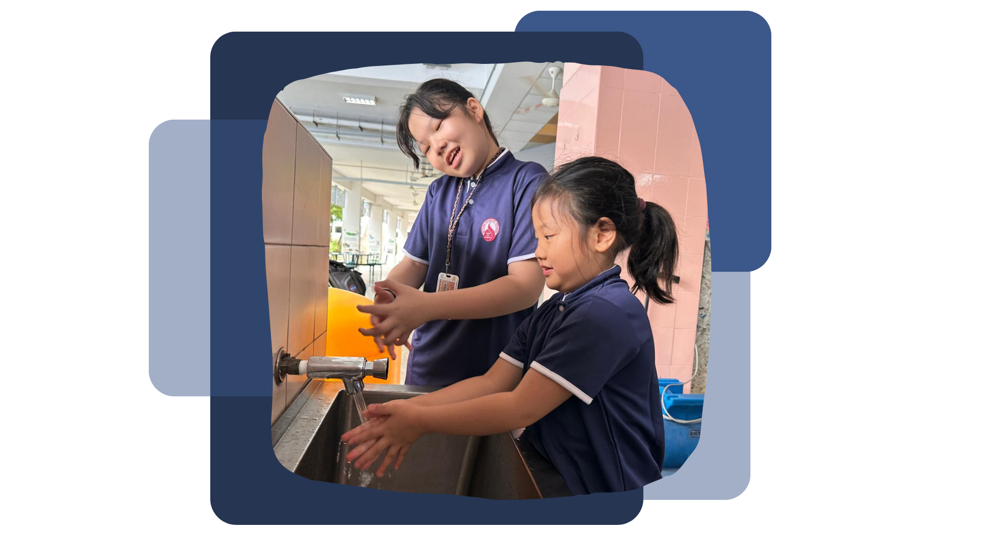 Two students in uniform washing hands together at a metal sink with running water in the canteen.