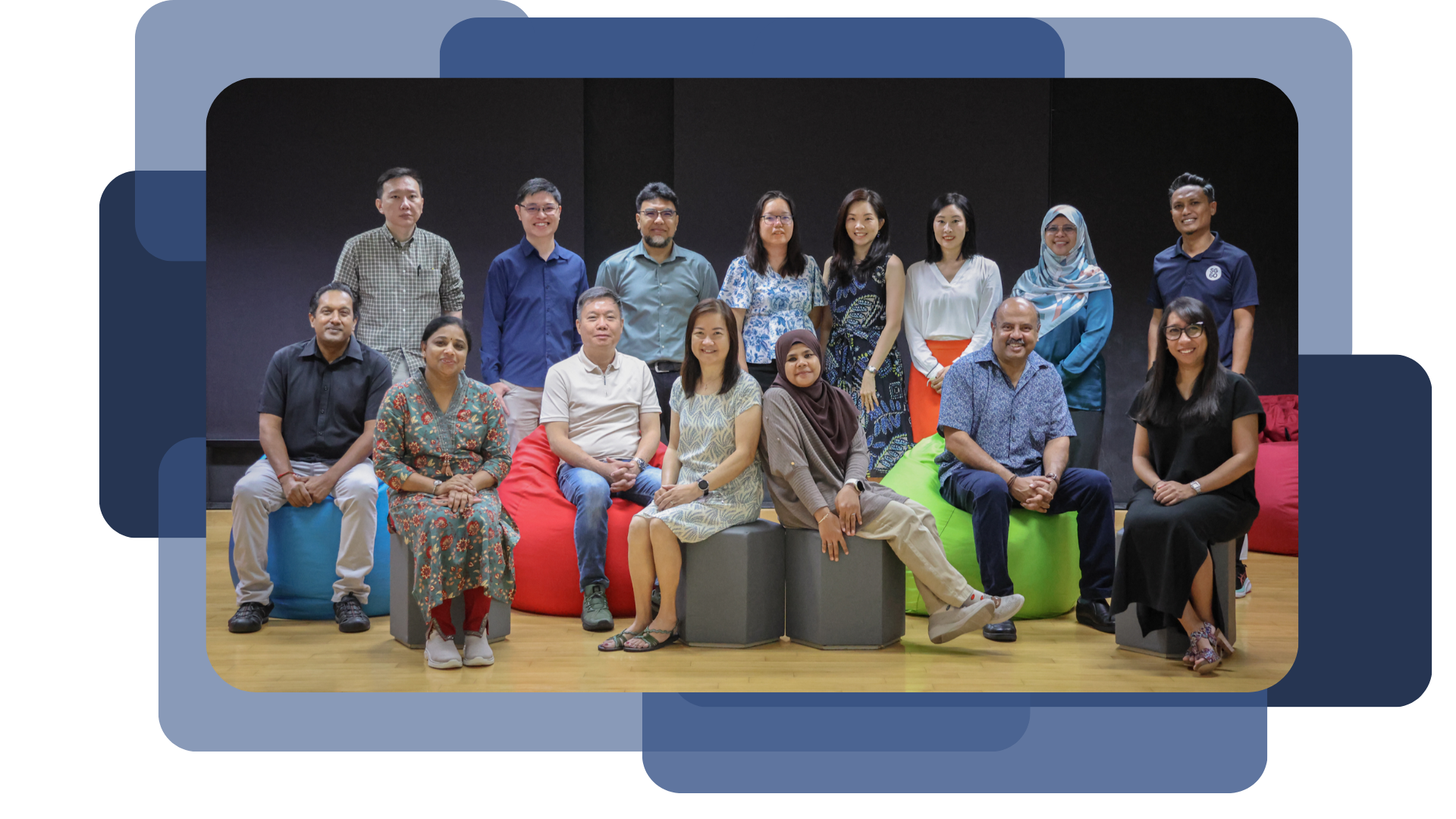 A group of about 15 people posing for a photo, some seated on colorful bean bags and stools, others standing behind.