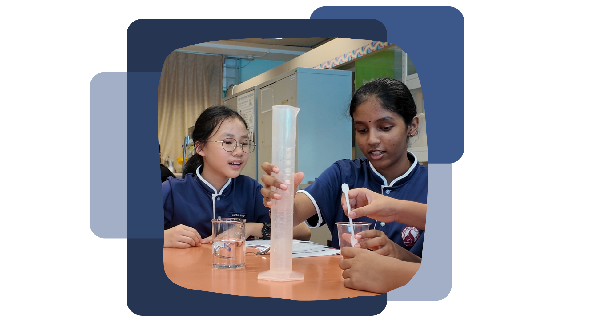 Two schoolgirls in blue uniforms conduct a science experiment with a measuring cylinder and beakers on a table.