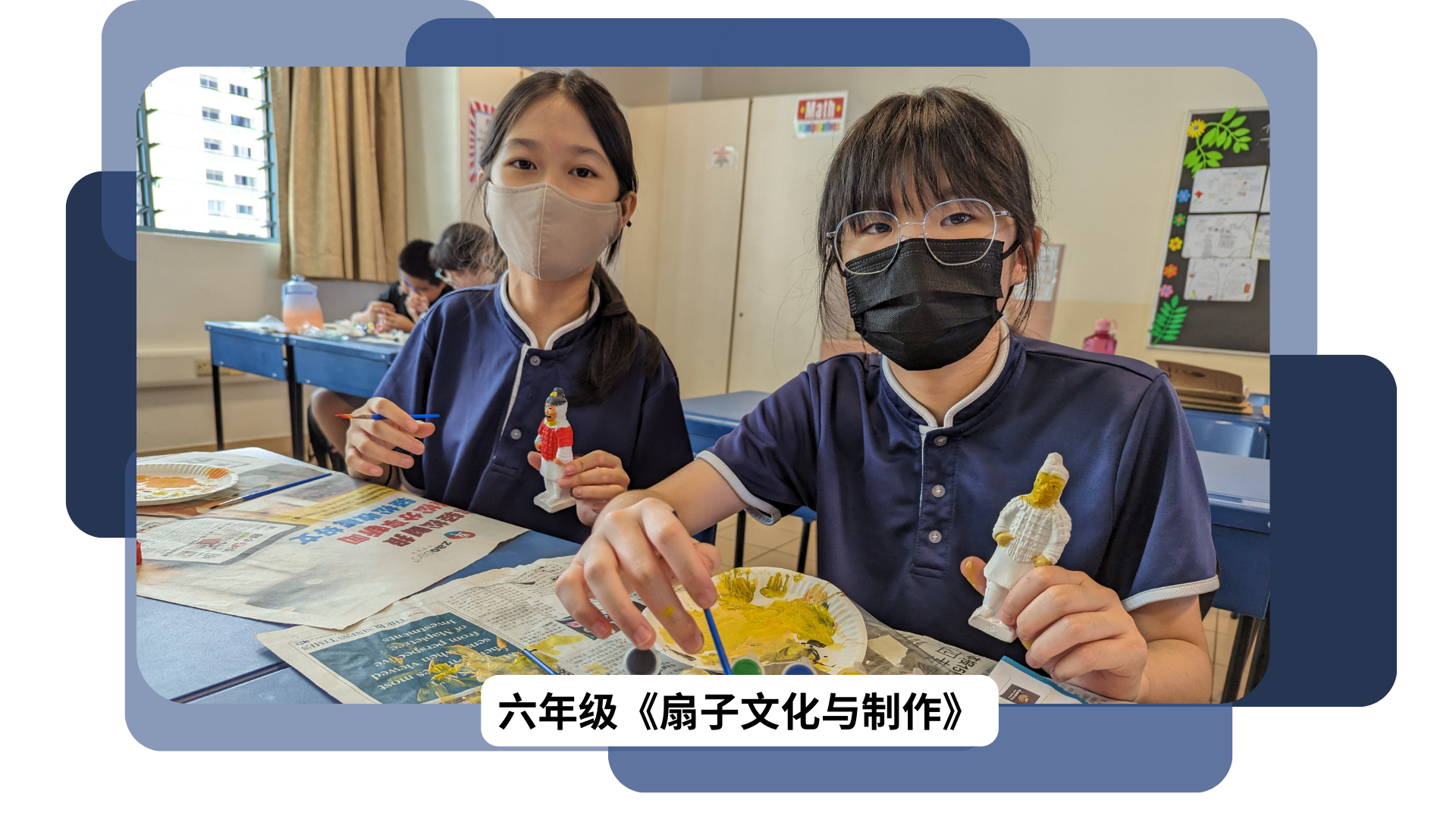 Two masked students in navy uniforms paint small figurines at a desk covered with newspaper in a classroom.