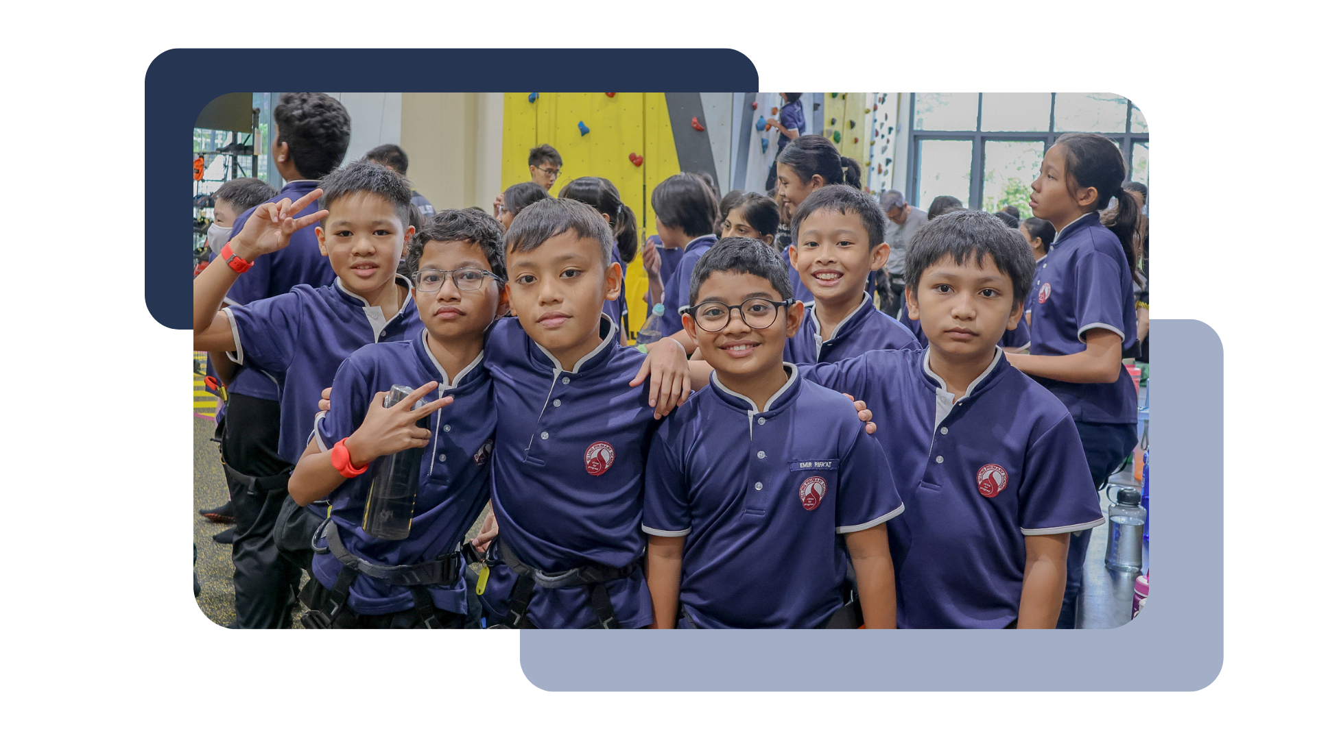A group of smiling boys in school uniforms pose together near a climbing wall indoors.