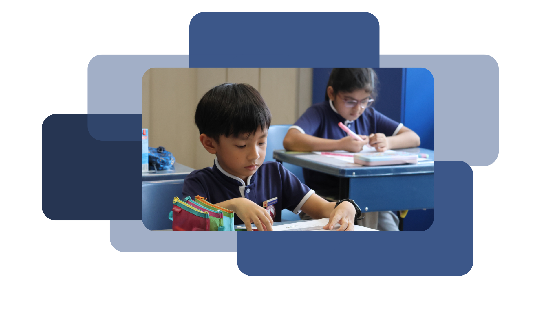 Two children in navy uniforms sit at school desks, focused on writing in notebooks.