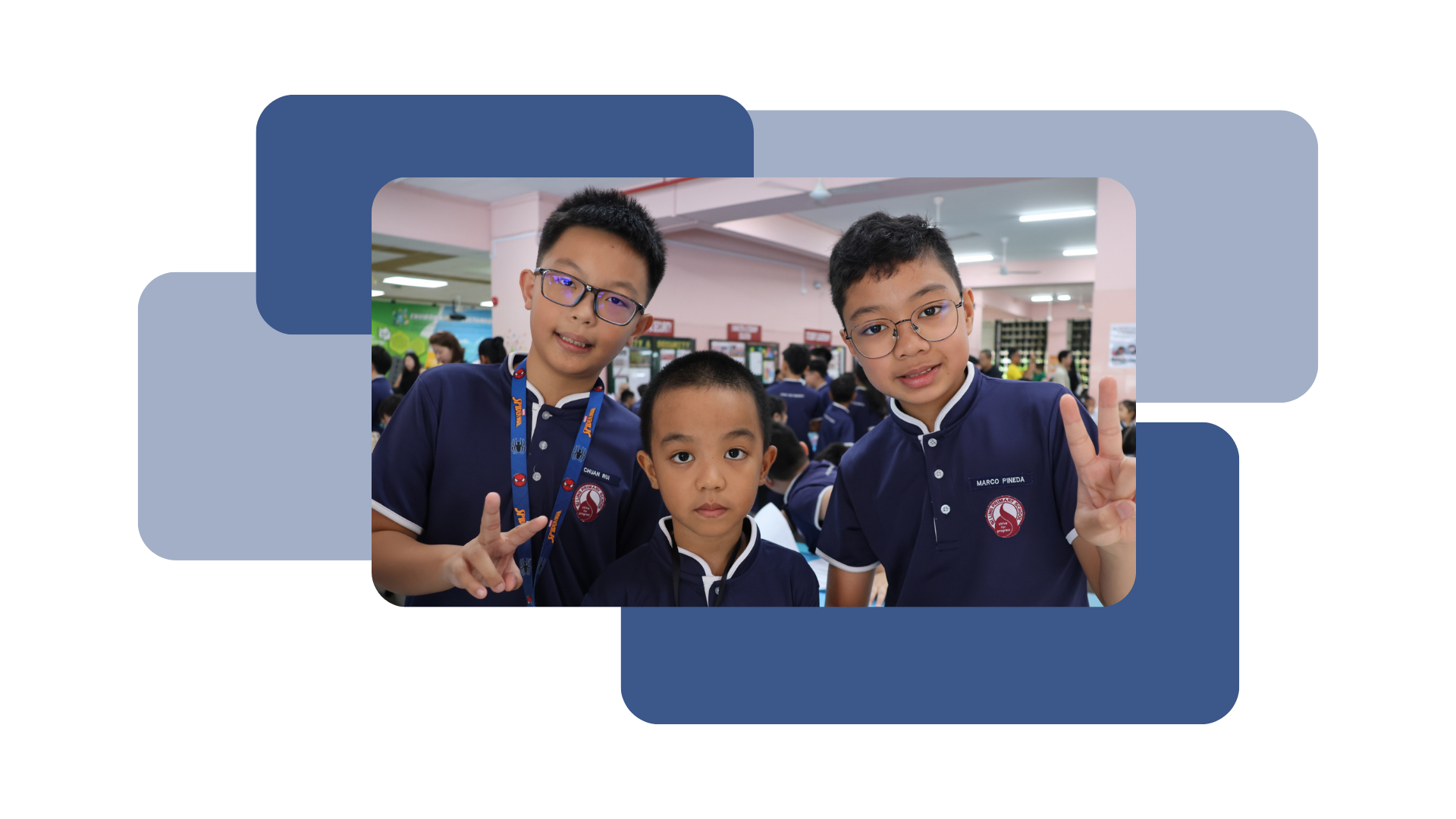 Three boys in school uniforms smile at the camera with two of them making peace signs, in the canteen.