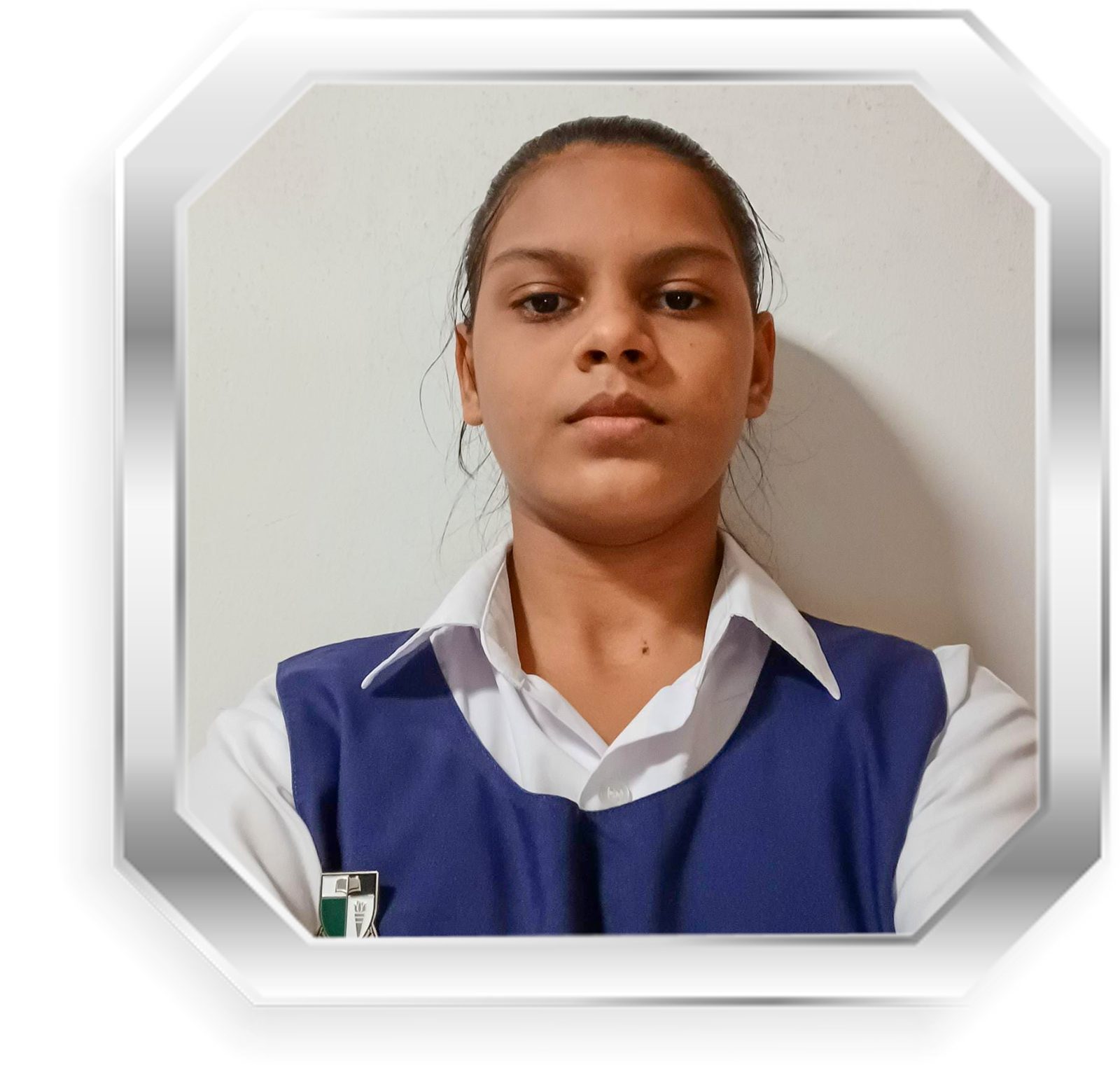 A young girl in a blue school vest over a white shirt with a badge, hair pulled back, facing forward.