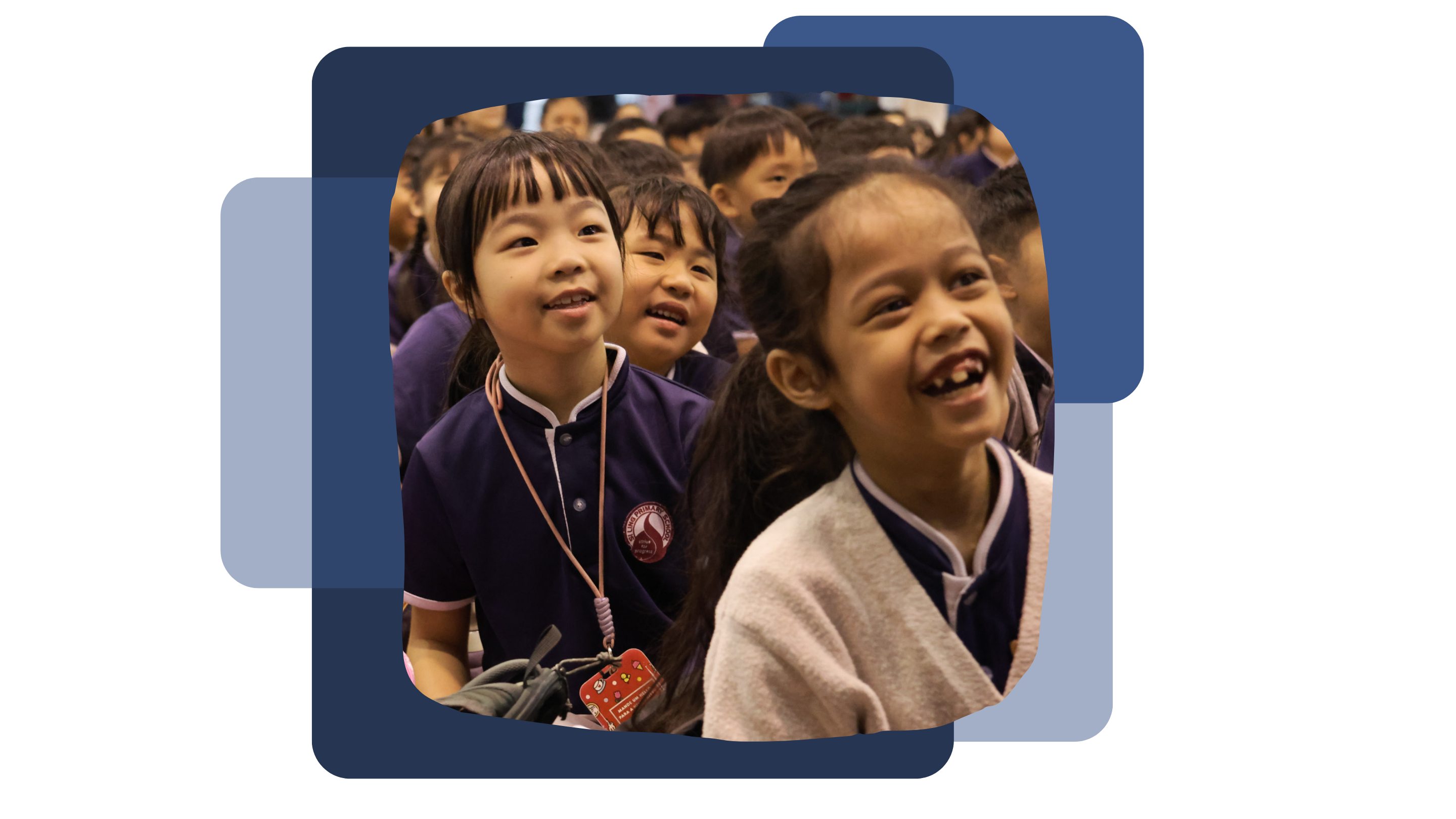 Primary One Students in their navy blue school uniforms, smiling and laughing while looking upward in a crowded school setting.