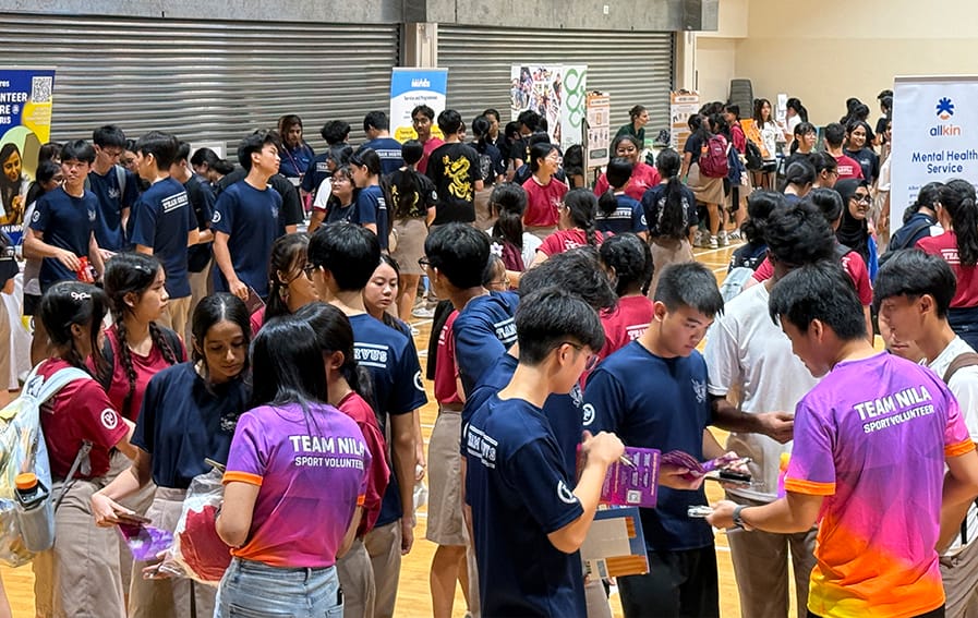 A busy school hall filled with students visiting community organisation booths, including Allkin Mental Health Service and Team Nila Sport Volunteer, during TM Connects 2026.