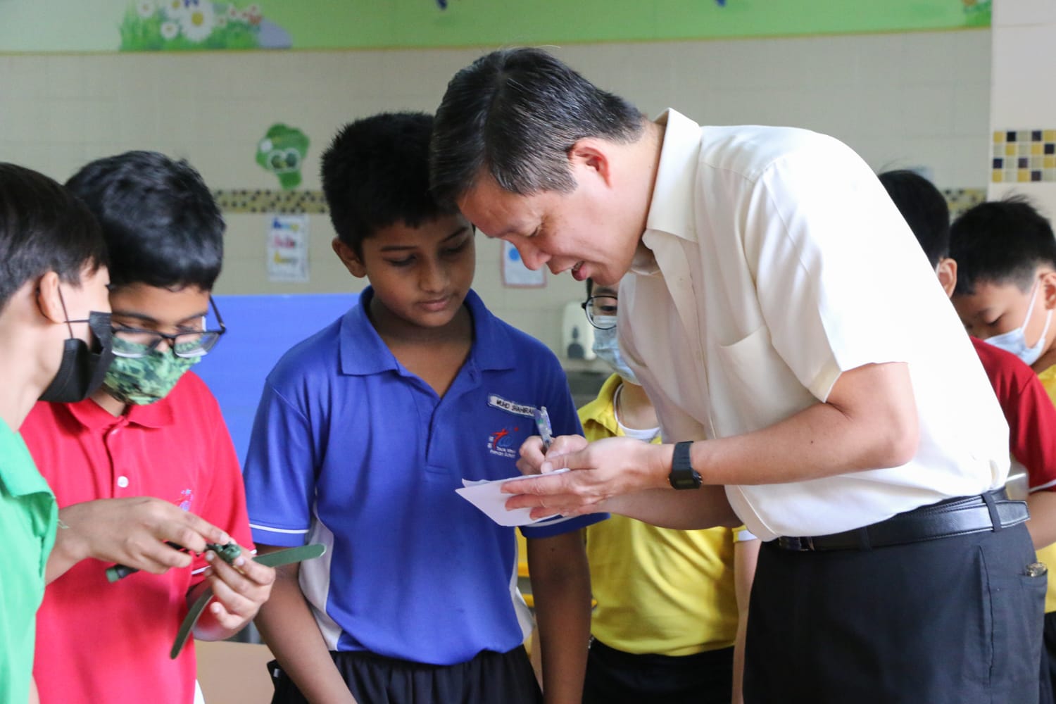 Minister Chan closely examined a student's Science and Technology Week project alongside a group of students.