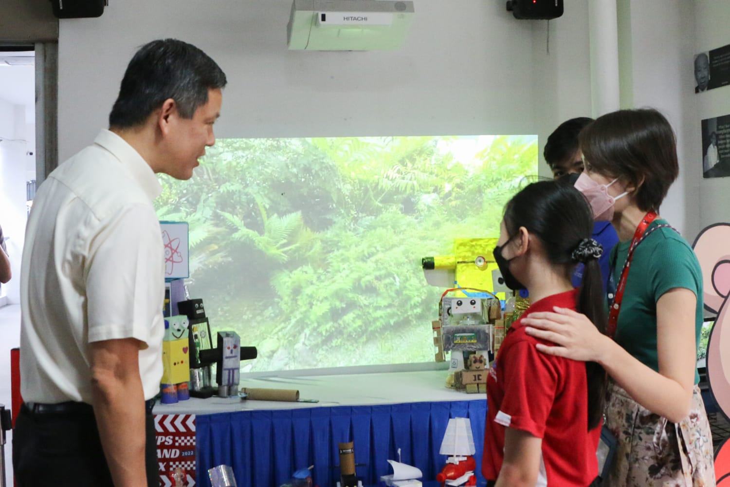Minister Chan viewing handmade robot models displayed by students during Science and Technology Week as a student explains her project.