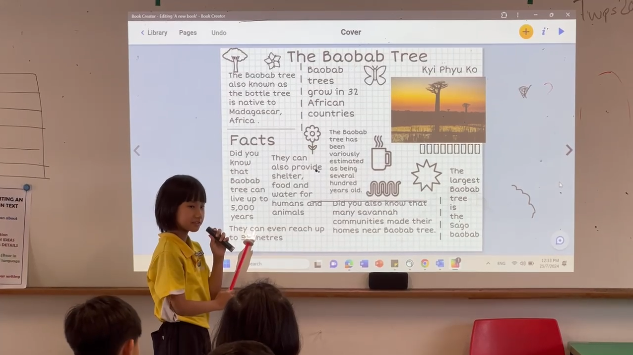 A young student in a yellow shirt presents a digital book about the Baobab Tree on a classroom projector screen.