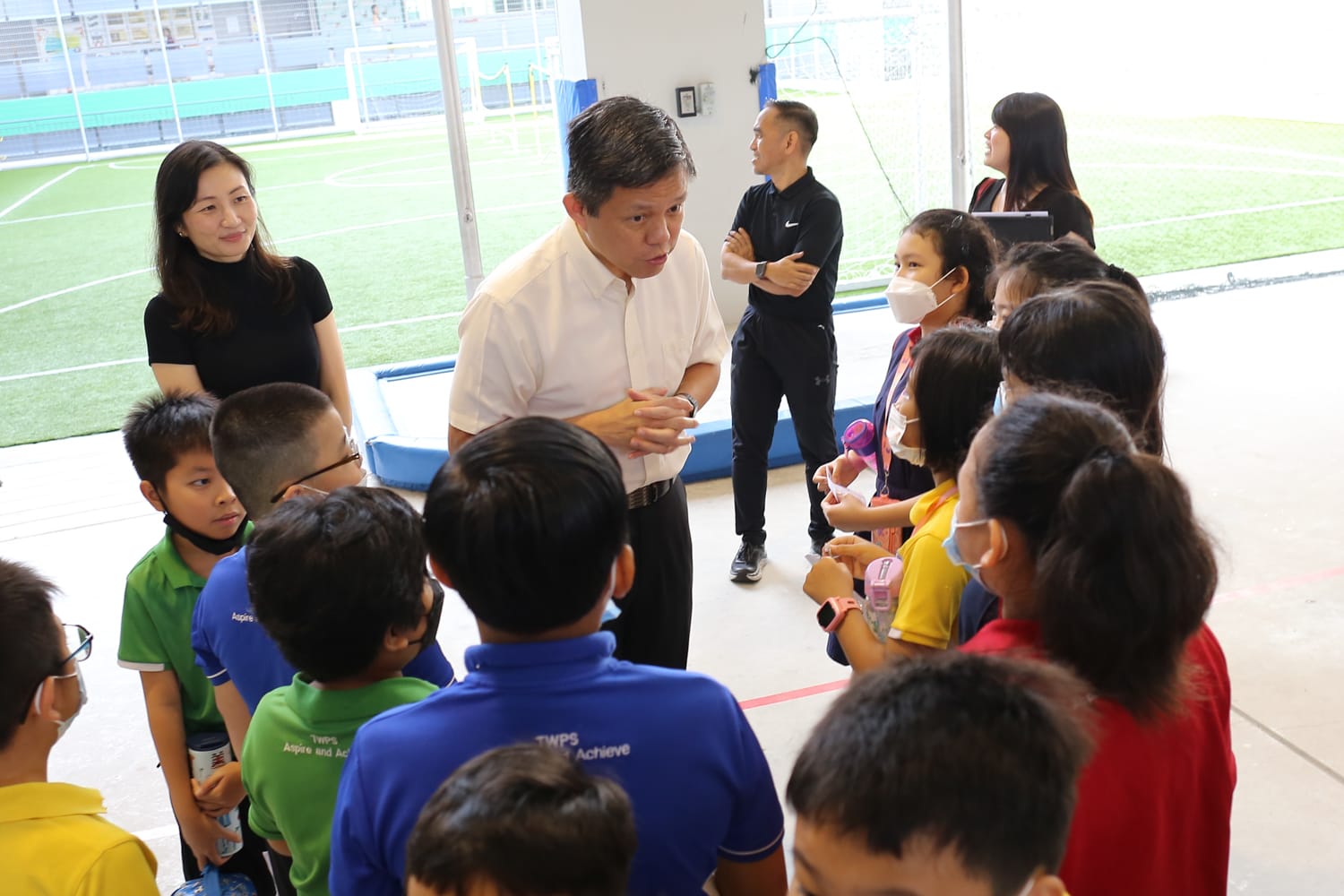 Minister Chan interacting with a group of students while staff members observe in the background. 