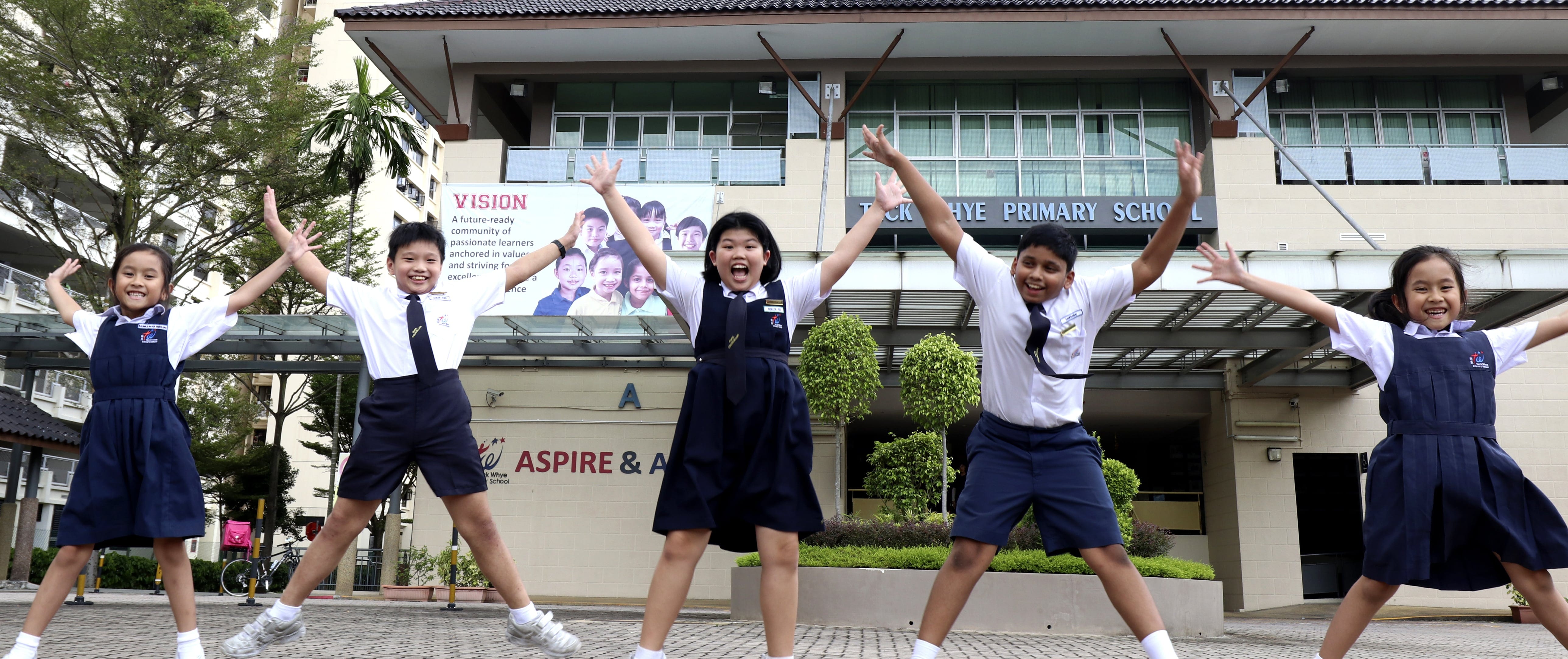 Photo of five student leaders jumping with their arms raised in front of Teck Whye Primary School.