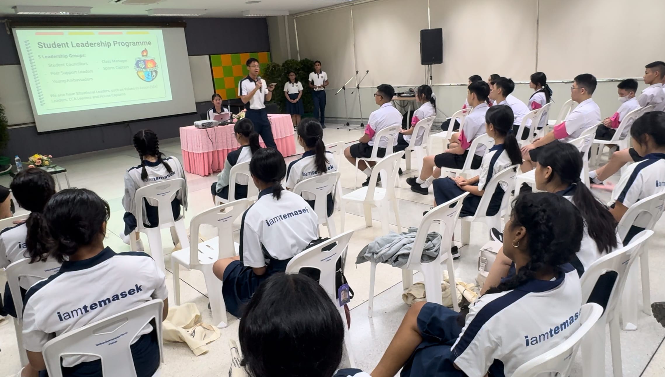 Students in iamtemasek uniforms sit in chairs facing a speaker presenting a Student Leadership Programme slideshow.