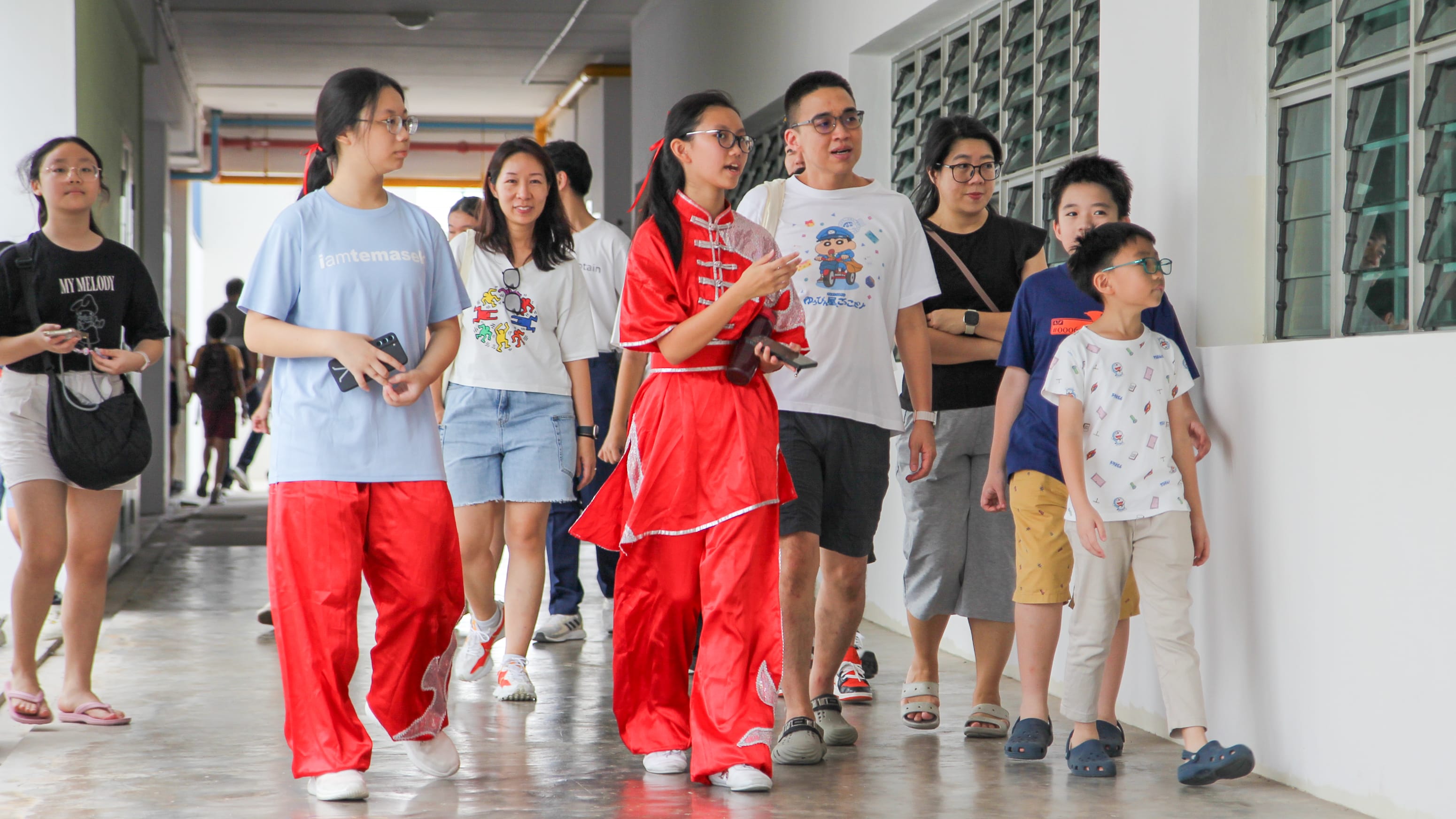 A group of people walking down a corridor, one woman wearing a red traditional Chinese outfit leading the group.