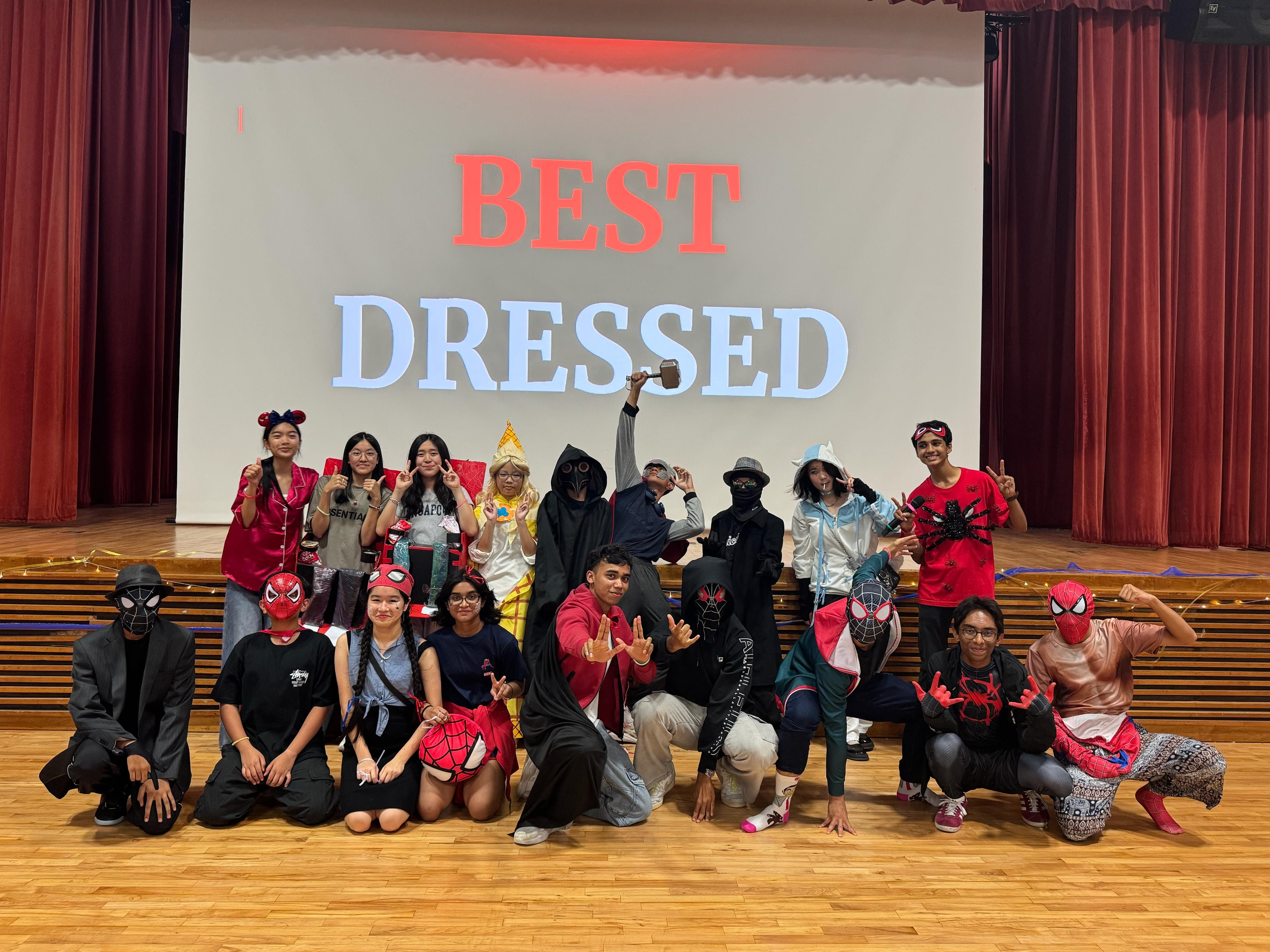 A group of students in costumes pose on a stage in front of a screen reading "Best Dressed."