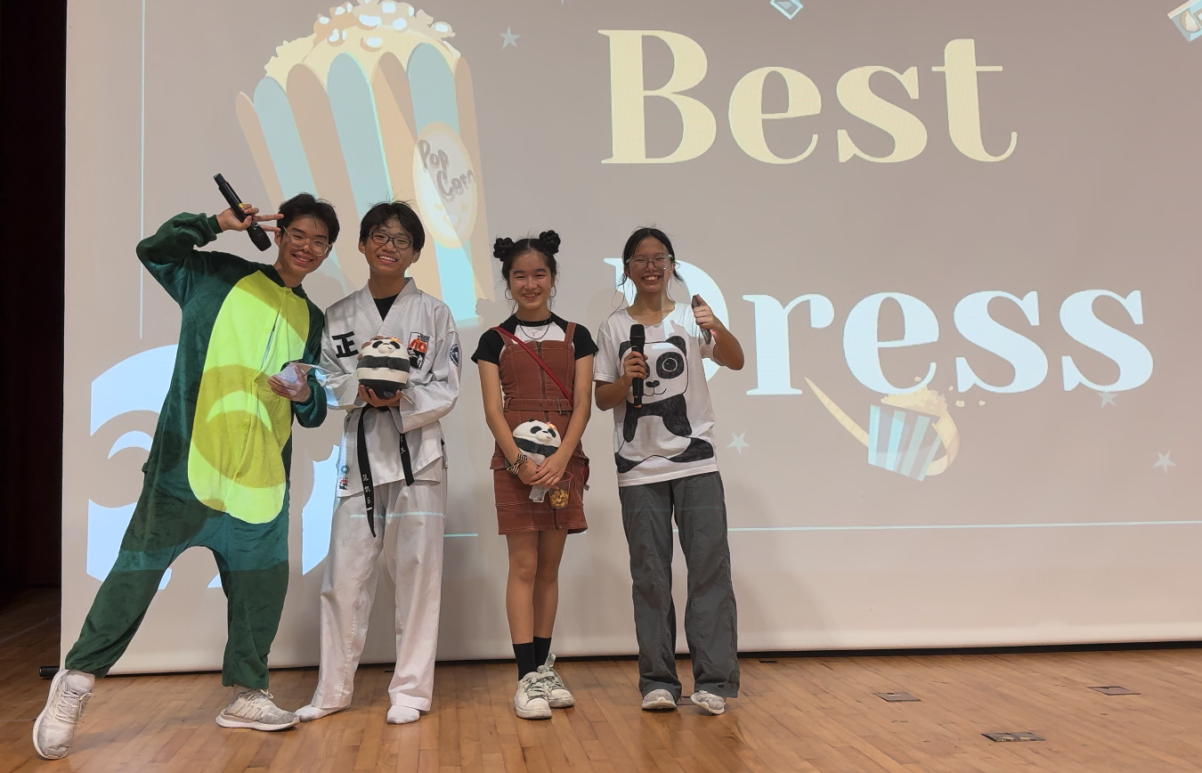 Four smiling teens in costumes stand on a stage in front of a projected screen reading Best Dress.