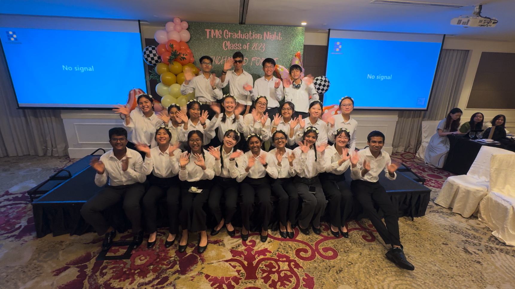 Group of students in white shirts waving at TMS Graduation Night Class of 2023 event with balloon decorations.