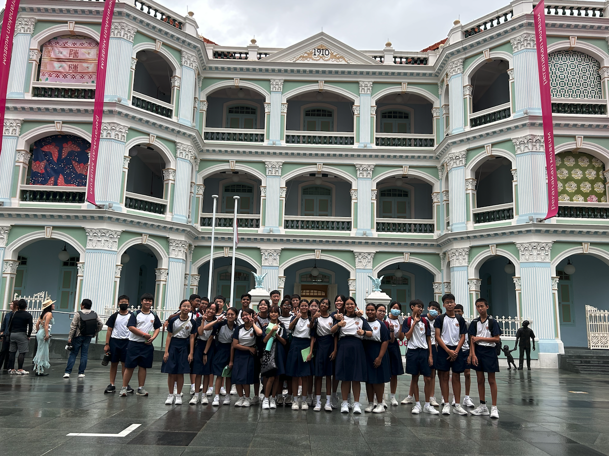 Students in school uniforms pose in front of the green colonial-style Peranakan Museum building dated 1910.